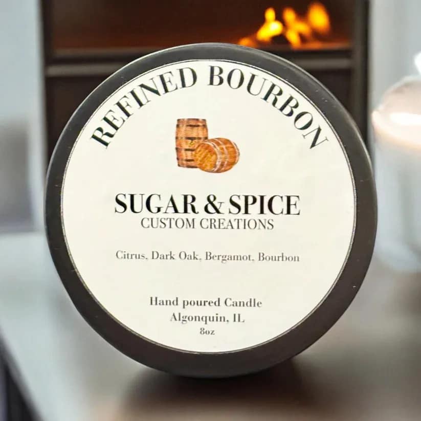 Round candle tin labeled Refined Bourbon with a lit flame in the background