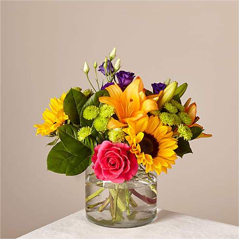 Mixed bouquet of sunflowers, roses, and lilies in a glass vase