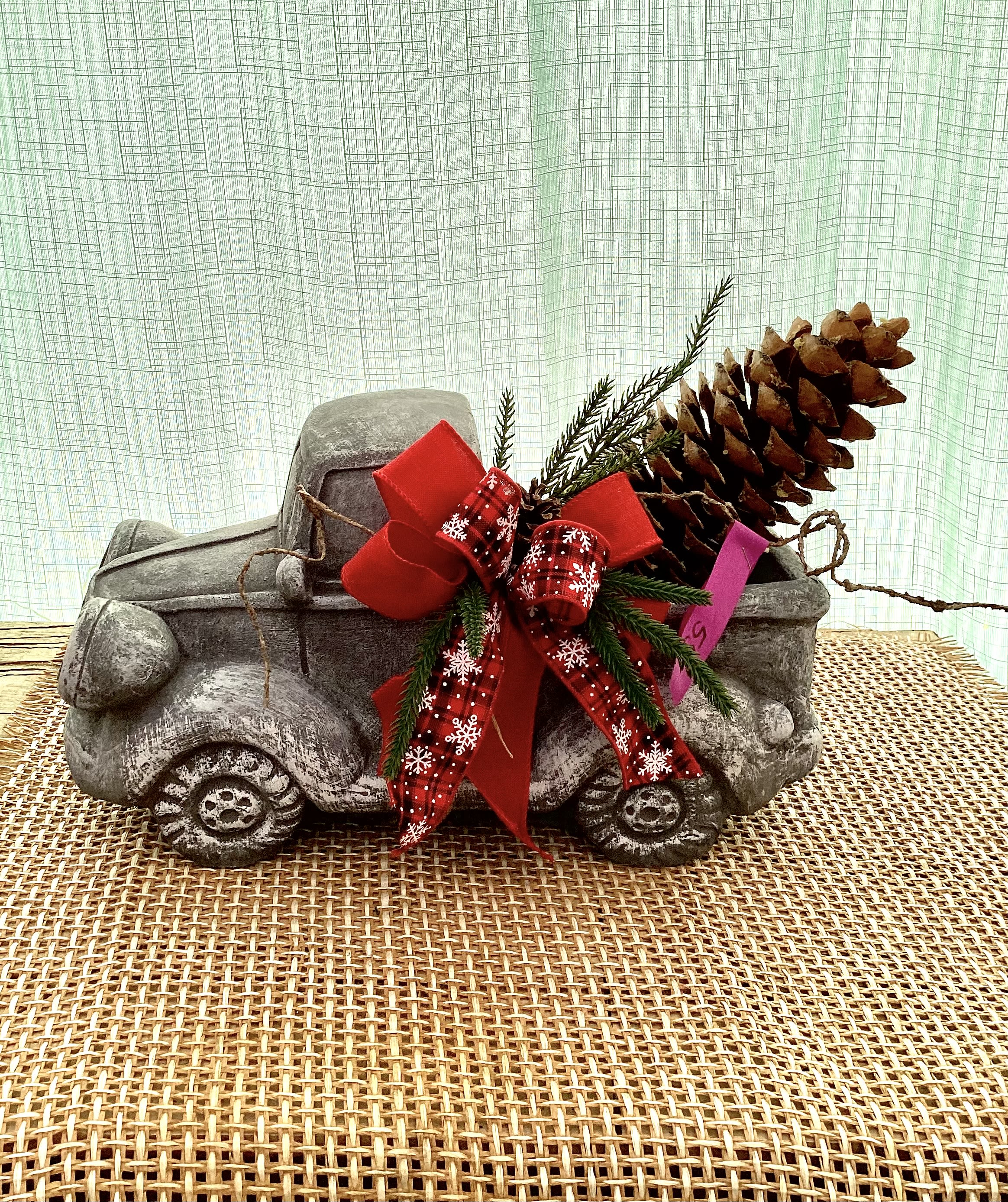 Decorative stone truck with a red holiday bow and pinecone accent