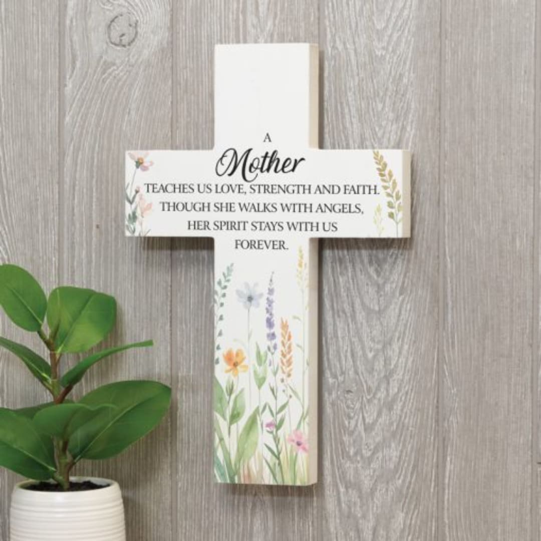 Decorative memorial cross sign with floral accents and a potted plant beside it