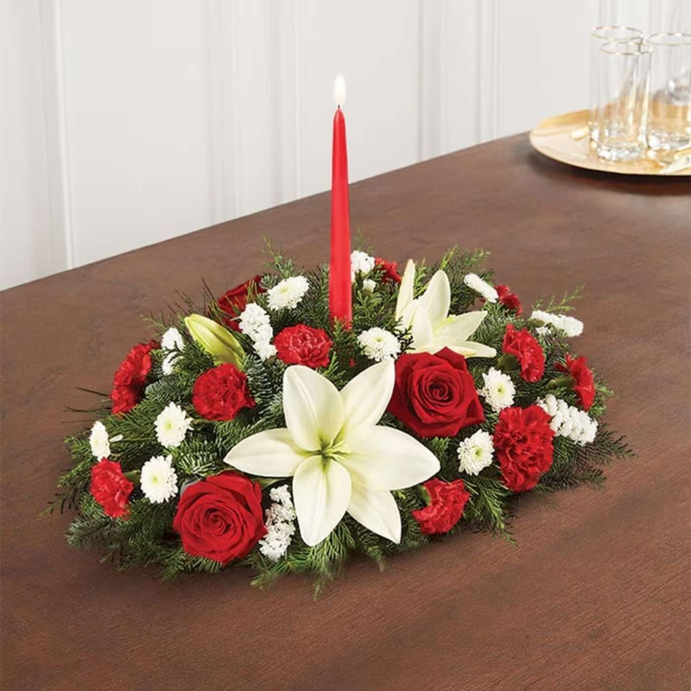 Traditional Christmas Centerpiece - Our classic table arrangement is an idyllic centerpiece for your Christmas celebration. Beautifully designed with long-lasting blooms in seasonal colors, this fragrant gathering features red taper candles to cast a warm, inviting glow throughout the holidays. Centerpiece arrangement with red roses, carnations, and mini carnations, and white Asiatic lilies, button poms, and statices, accented with assorted Christmas greenery