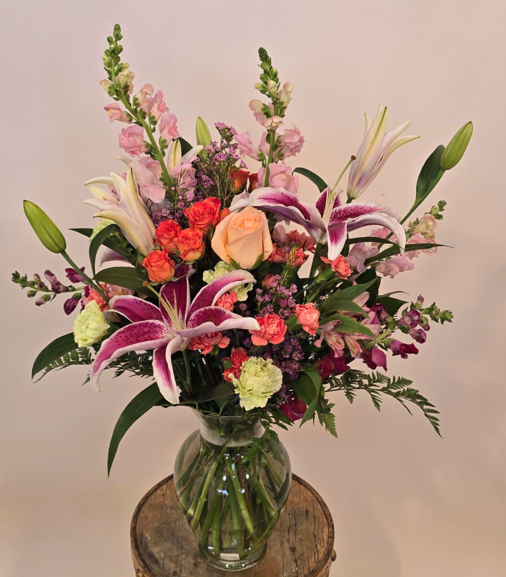 Tall mixed bouquet with pink lilies, roses, carnations, and snapdragons in a clear glass vase