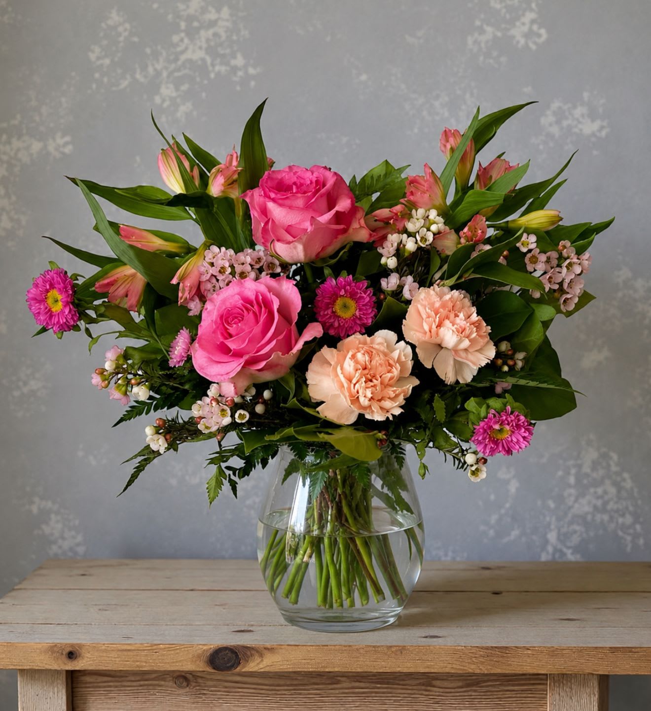 Blush Rush  - Blush Rush is a cheerful burst of hot and soft pinks designed to brighten the day without overwhelming the room.   Blush-toned blooms are artfully mixed with fresh greenery to create a look that feels light, happy, and just a little playful.   Perfect for sending a smile, lifting spirits, or simply celebrating someone’s love for all things pink, this arrangement is proof that a gentle pop of color can make a big difference.