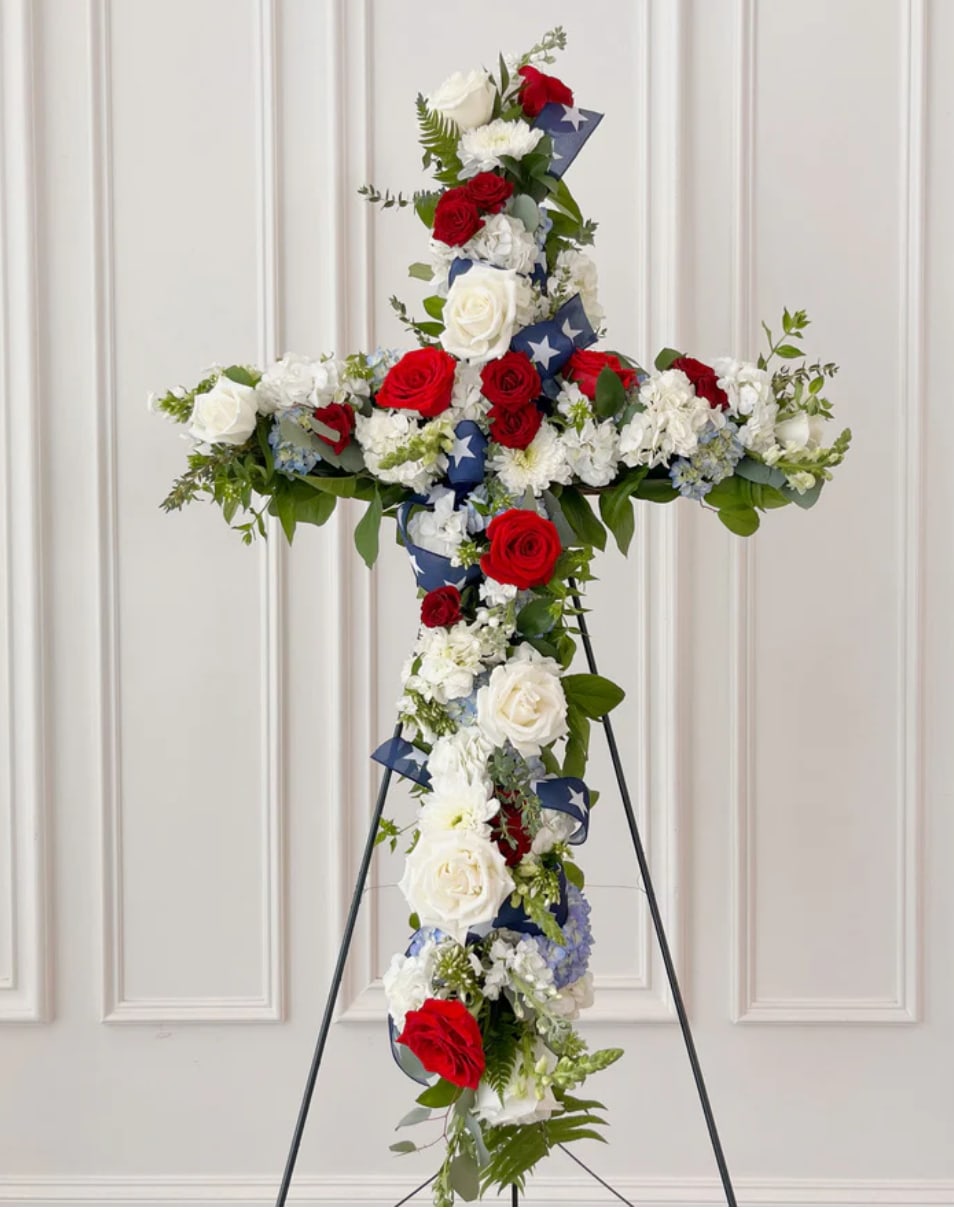 Dearly Patriotic - Standing Cross -  In memory of our Veterans and First Responders. This arrangement is a beautiful tribute to honor our Veterans and First Responders. Filled with lush greenery and fragrant blooms, this funeral arrangement is a stunning and meaningful way to pay respects. 