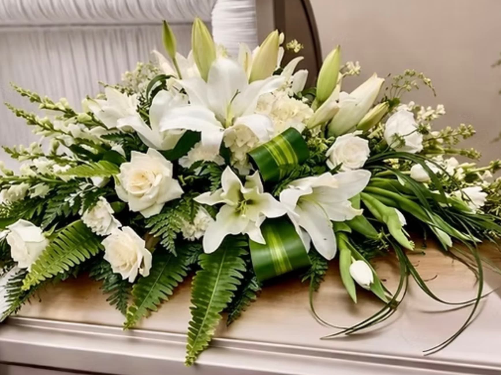 White lilies and roses arranged in a low casket spray