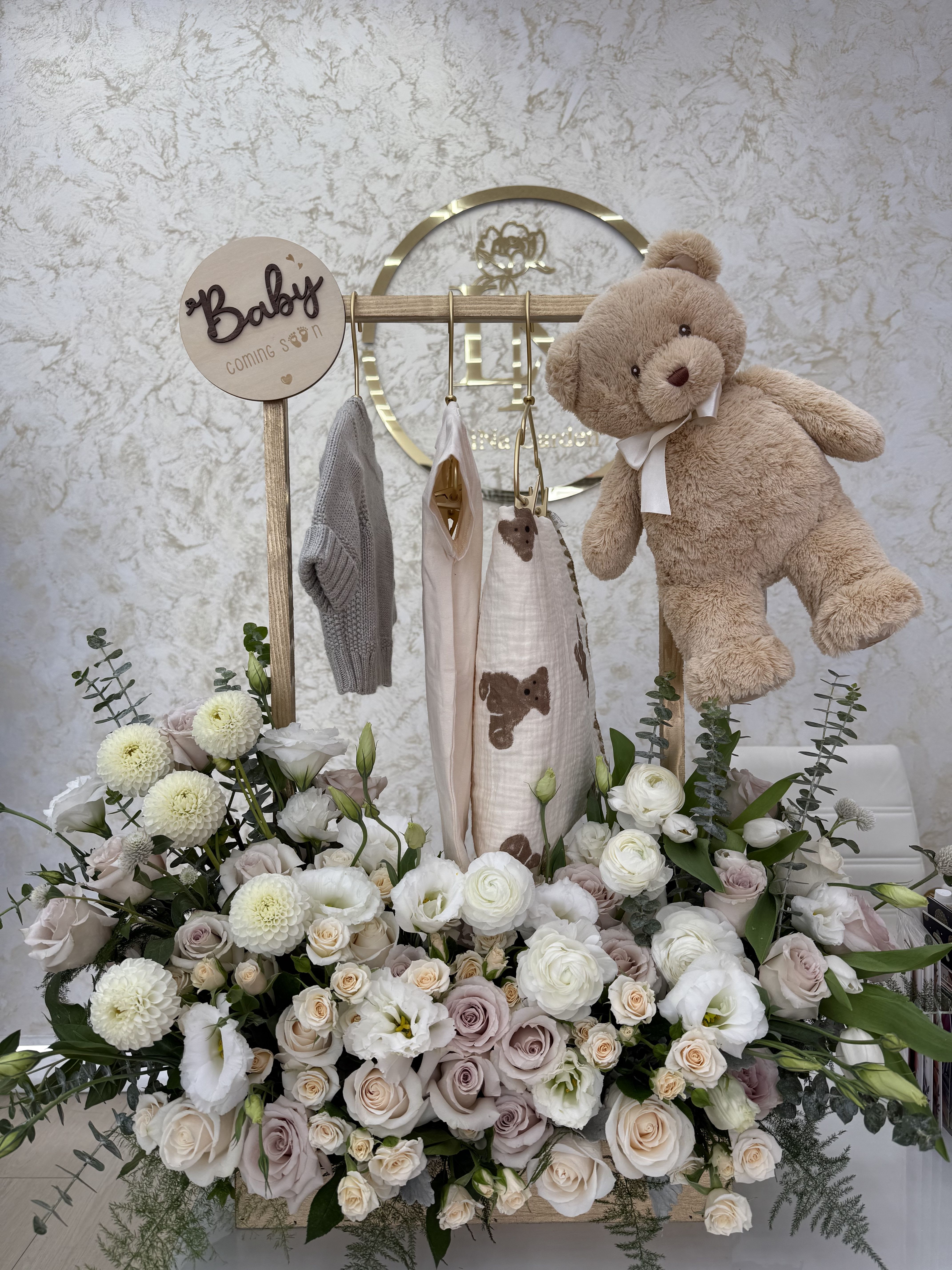 Baby shower floral display with a teddy bear and hanging baby clothes