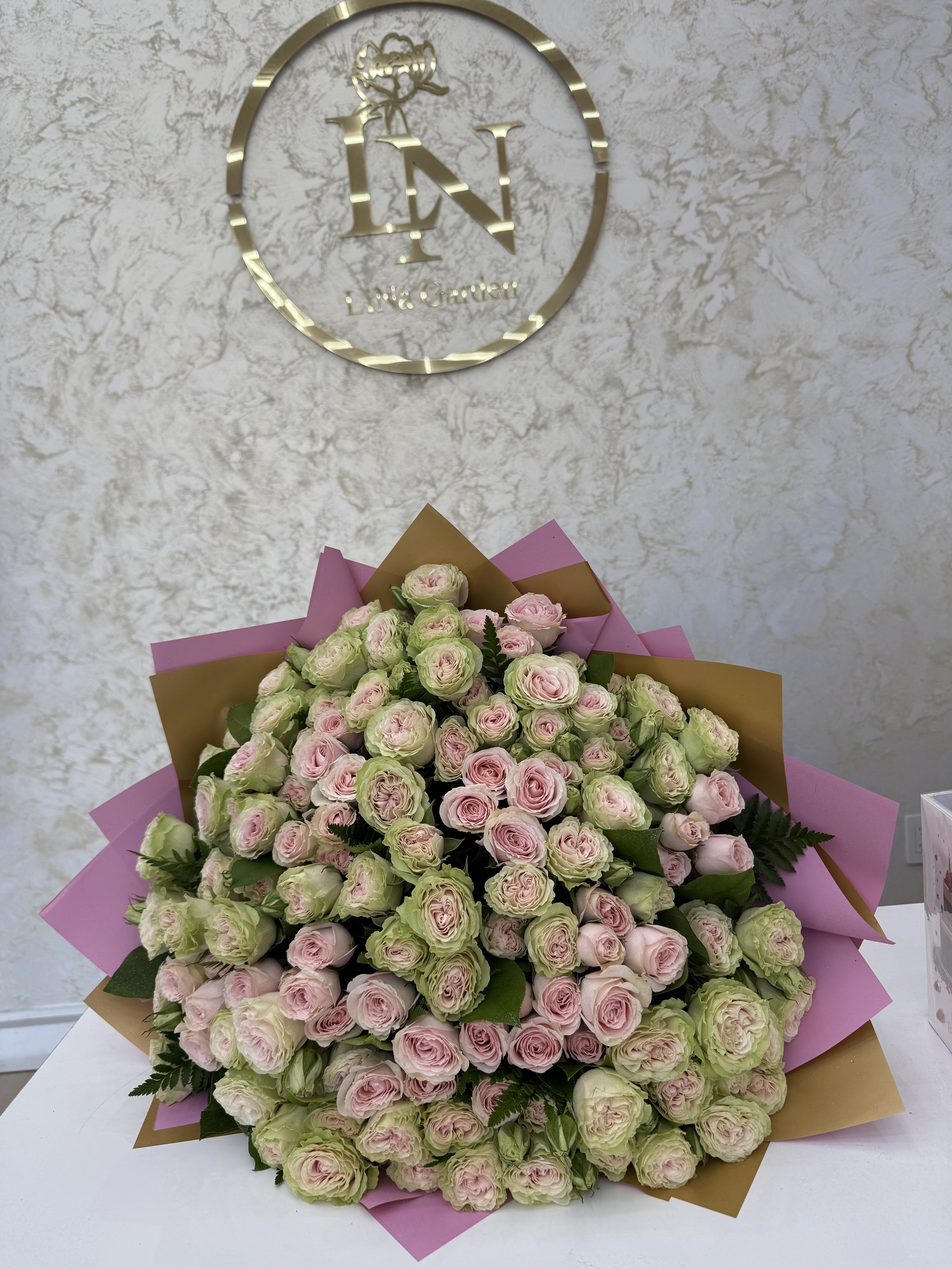 Large bouquet of pale pink and green roses wrapped in pink and gold paper