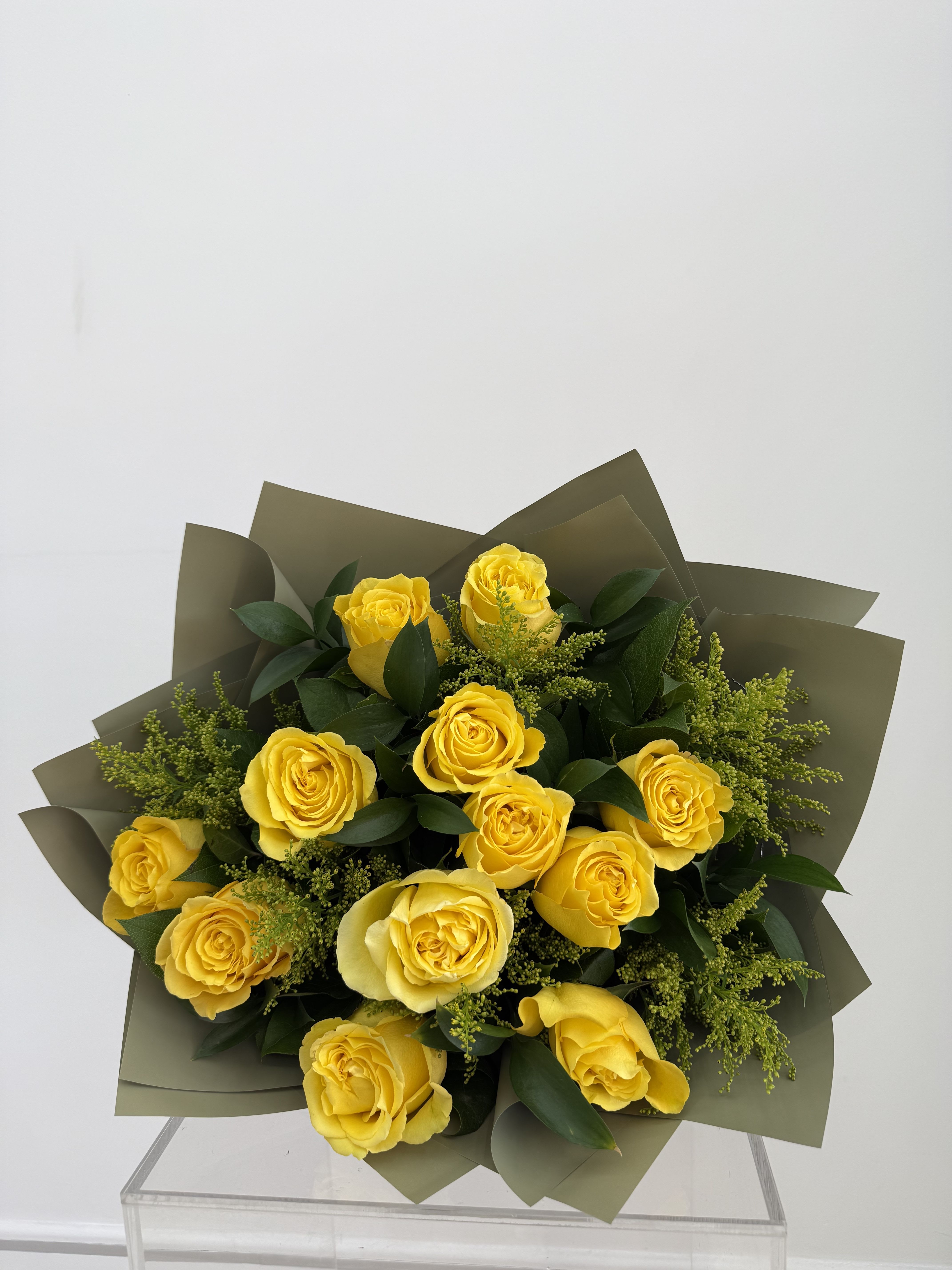 Bouquet of yellow roses with dark green foliage and olive wrapping