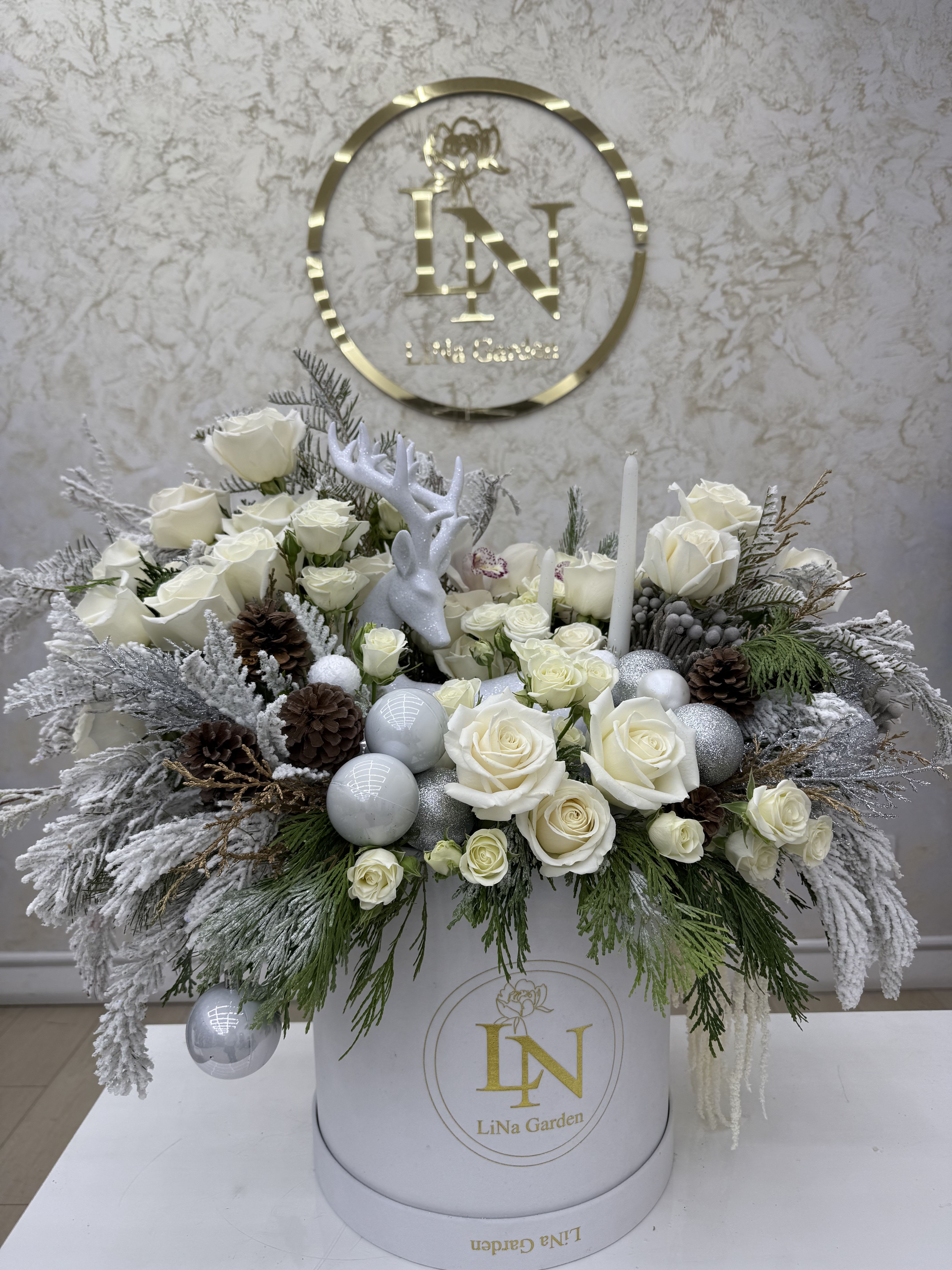 White rose arrangement in a round box with silver ornaments and pinecones