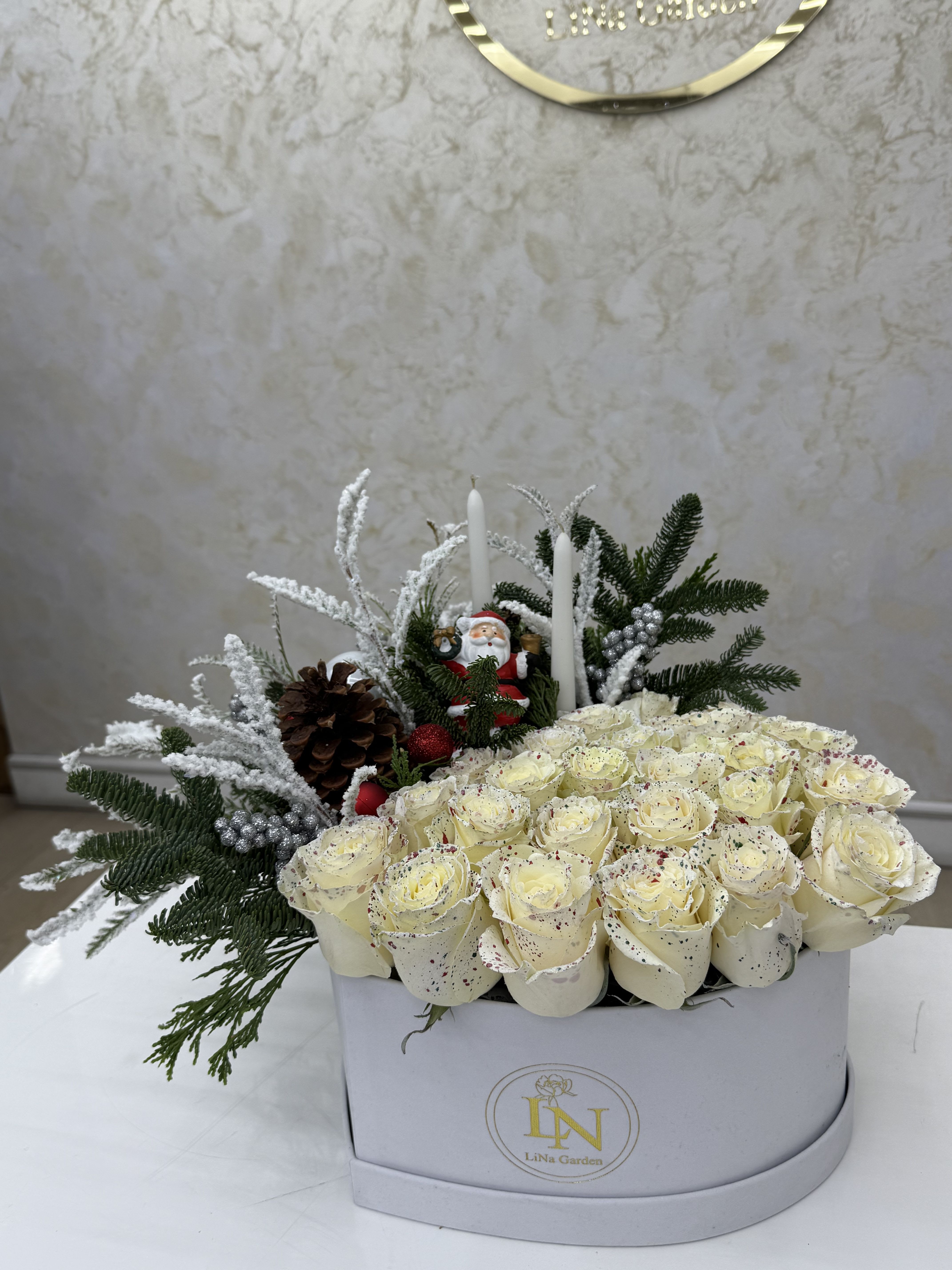 White roses in a box with pine, candles, and a Santa figurine
