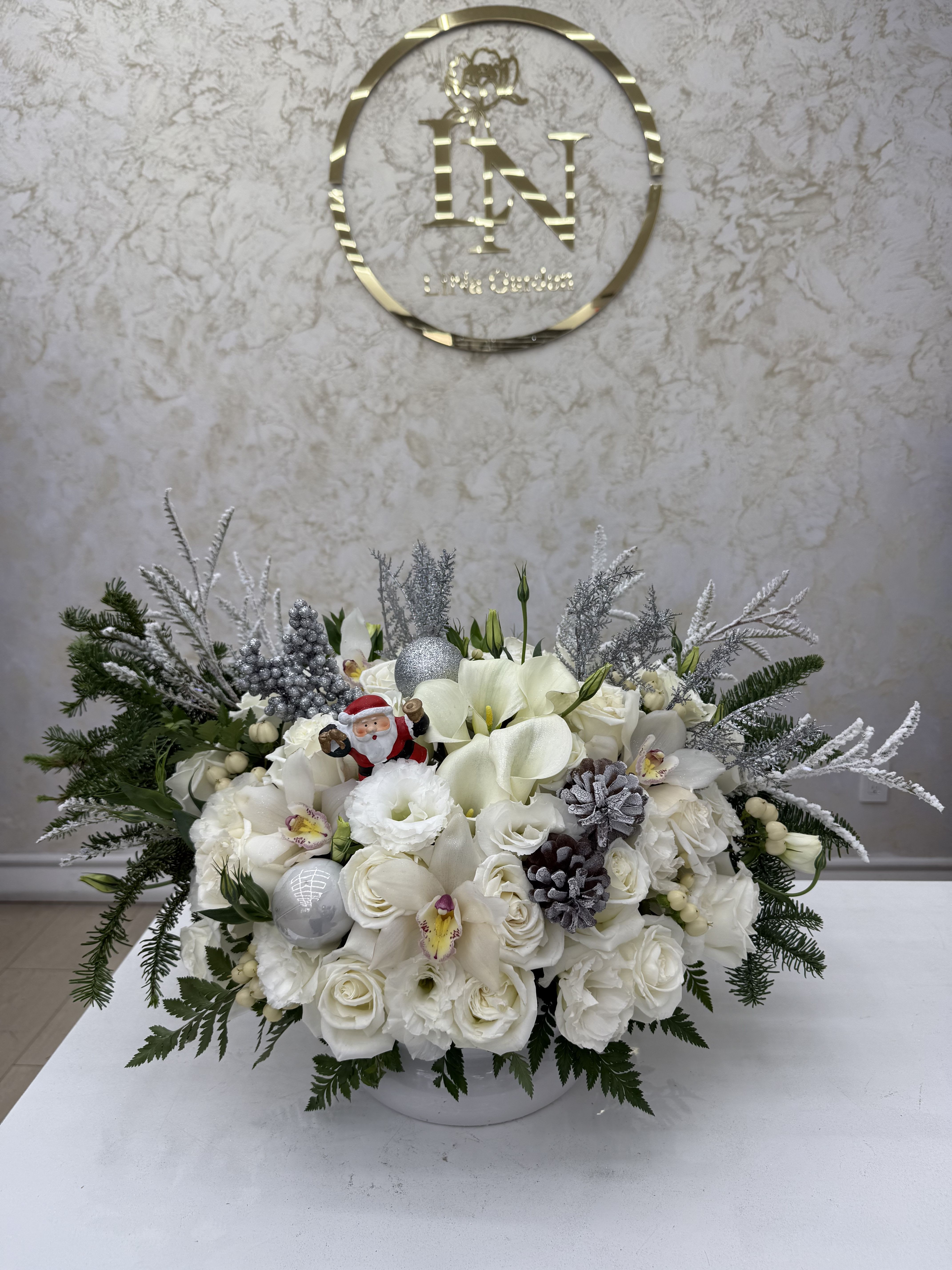 White floral arrangement with holiday ornaments and evergreen accents in a low container