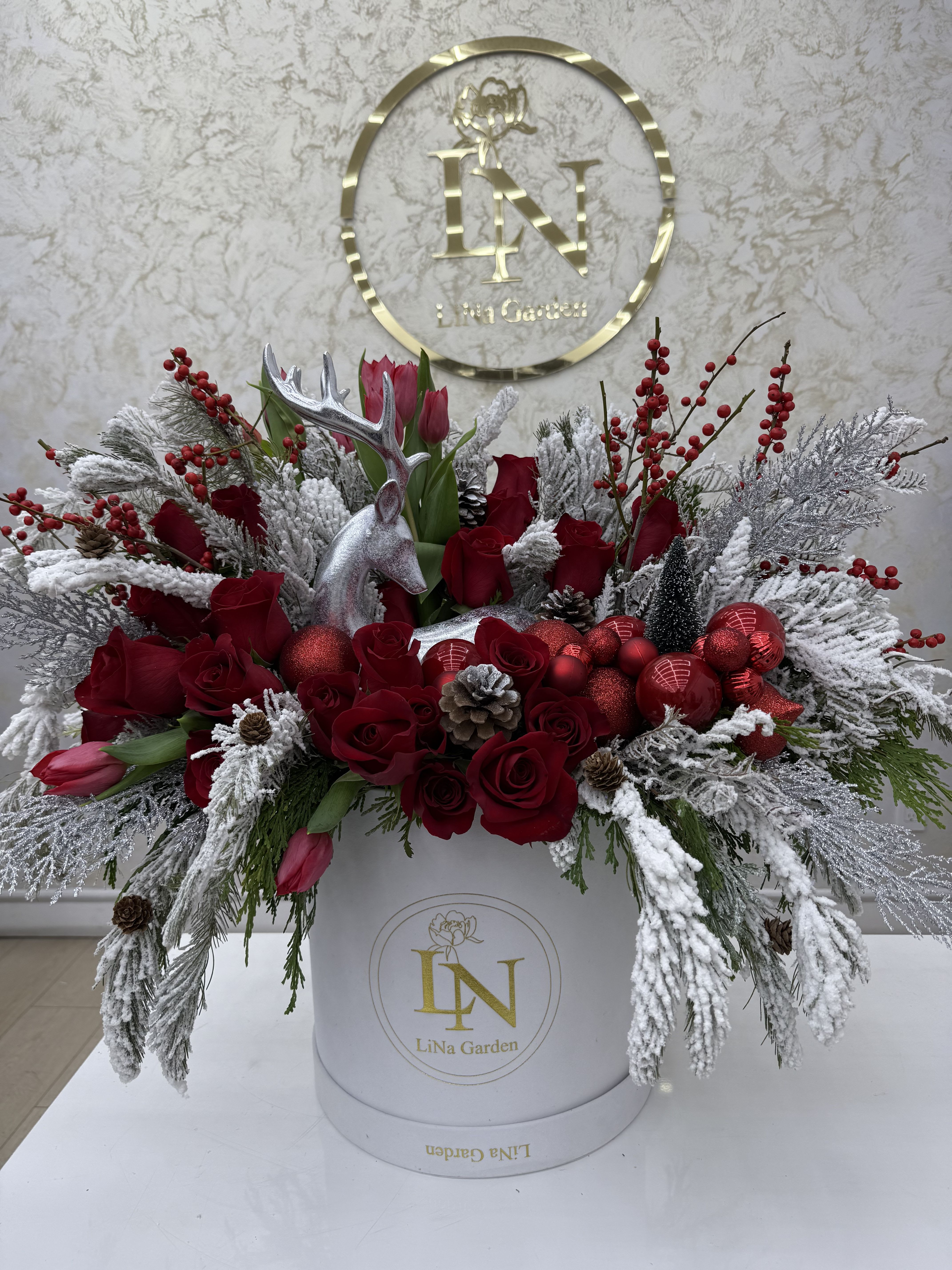 Red roses and tulips arranged with frosted branches in a white box