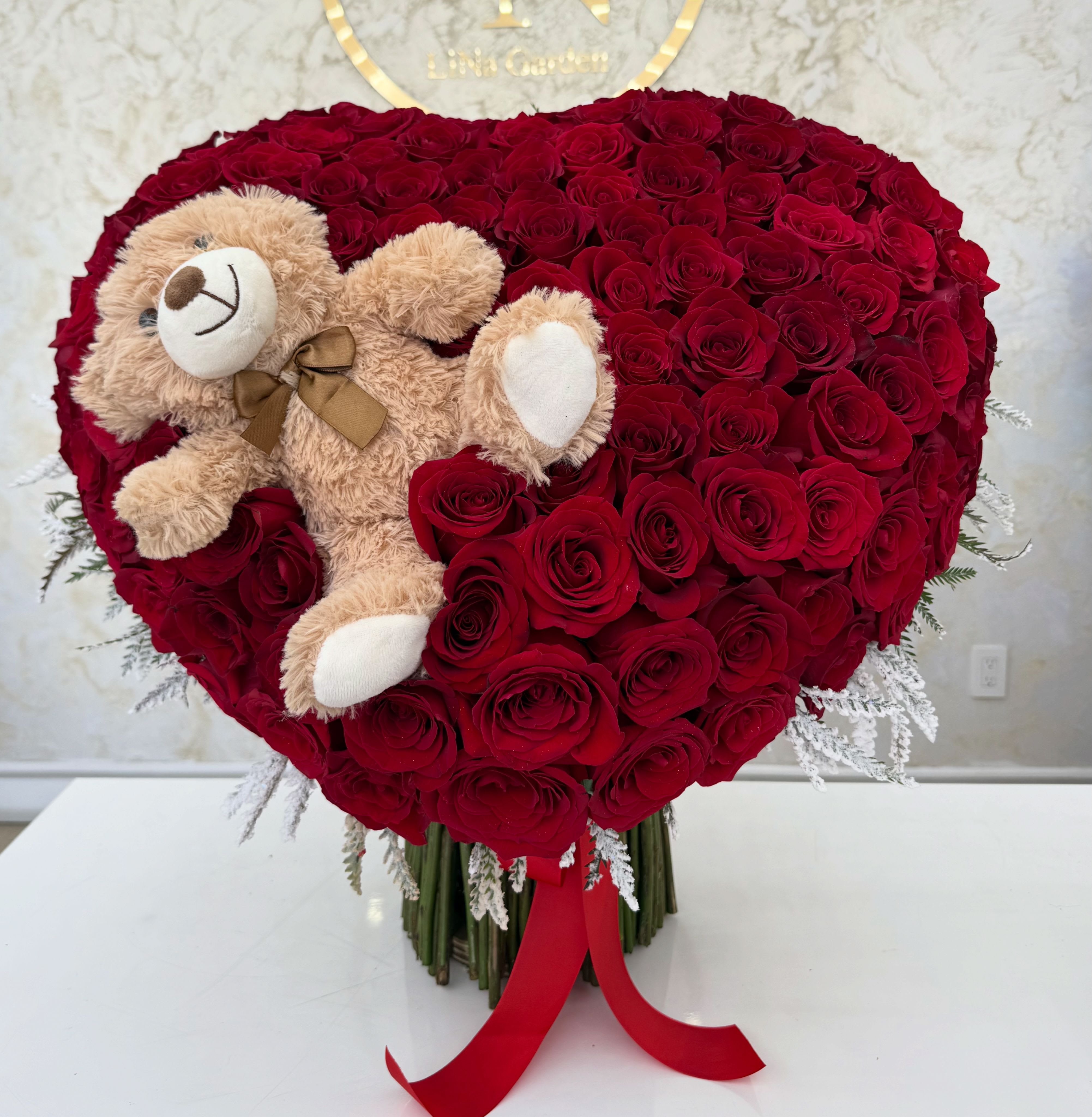 Heart-shaped red rose arrangement with a teddy bear and red ribbon