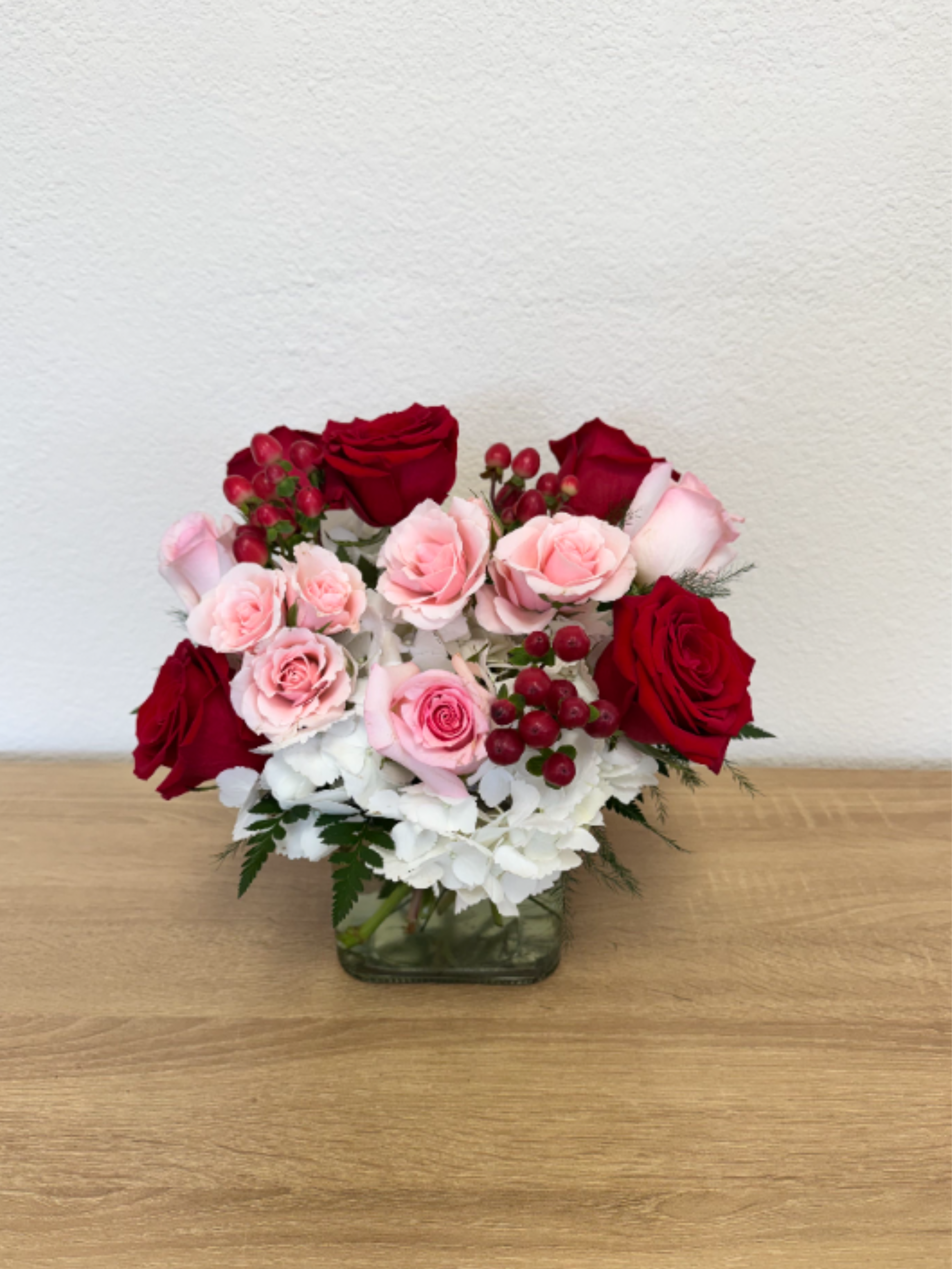 Blushing Love  - Cube arrangement with white hydrangea, red roses, pink roses, pink spray roses and red hypericum berry.  