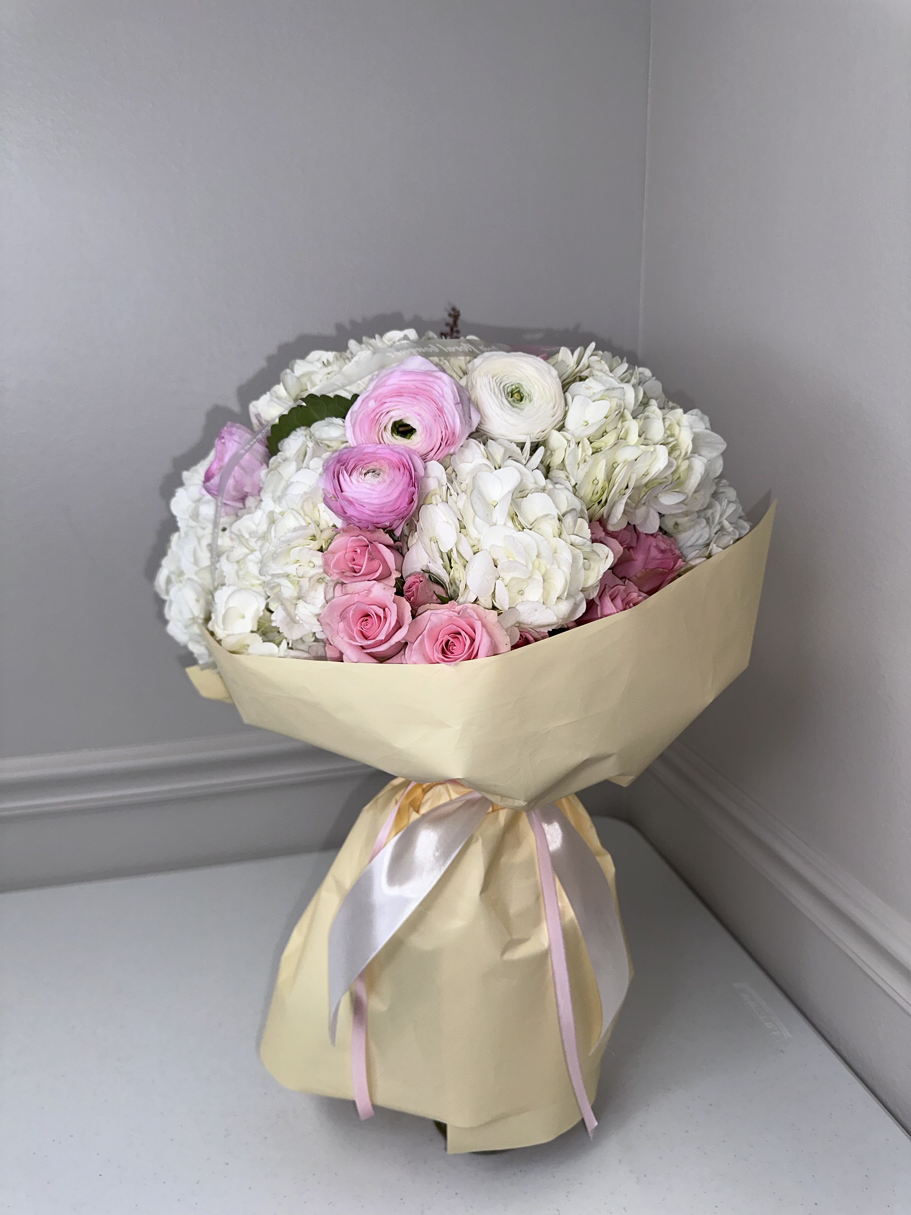 Bouquet of pink and white flowers wrapped in beige paper with ribbon