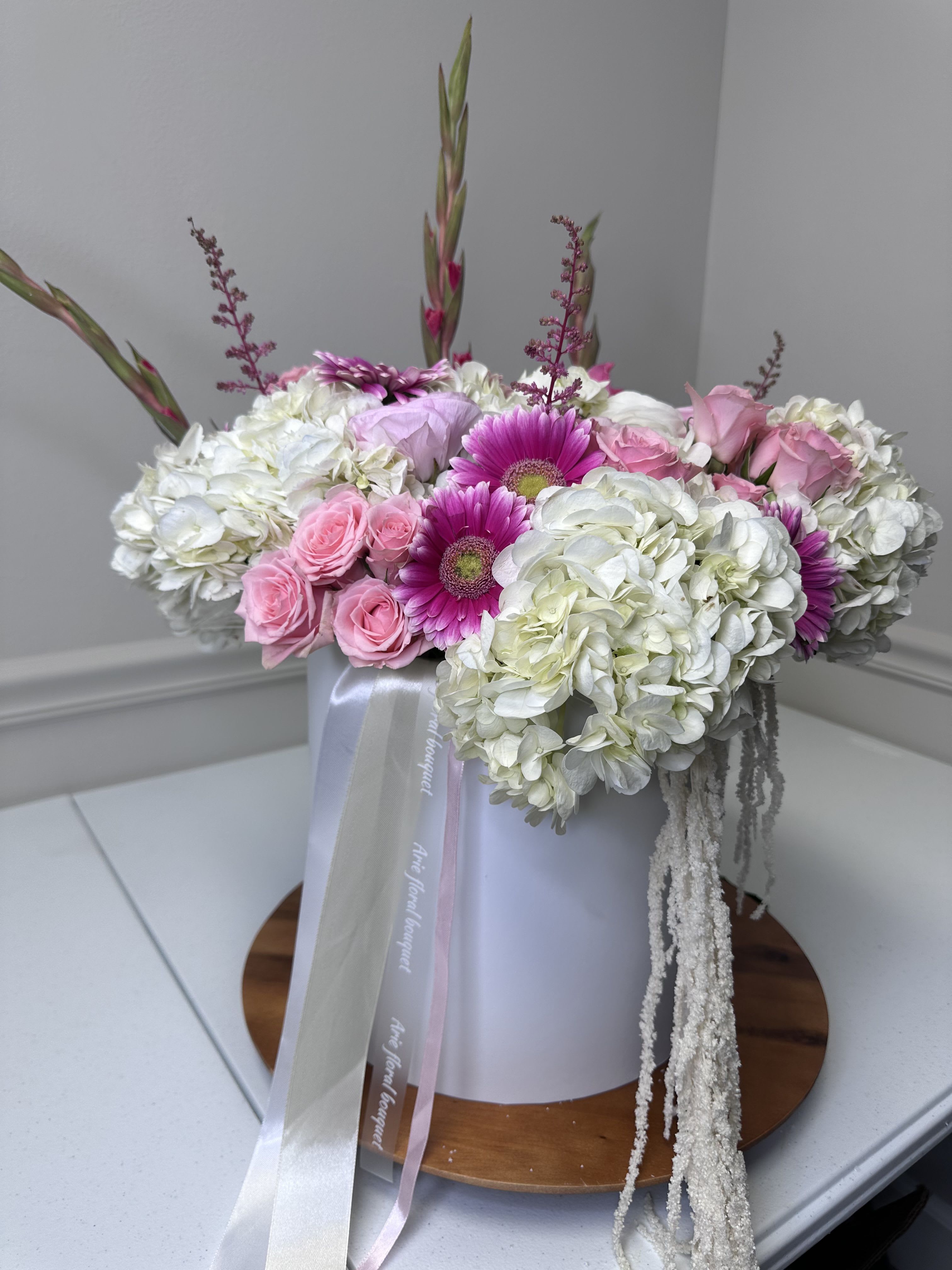Pink roses and magenta daisies arranged with white hydrangeas in a box