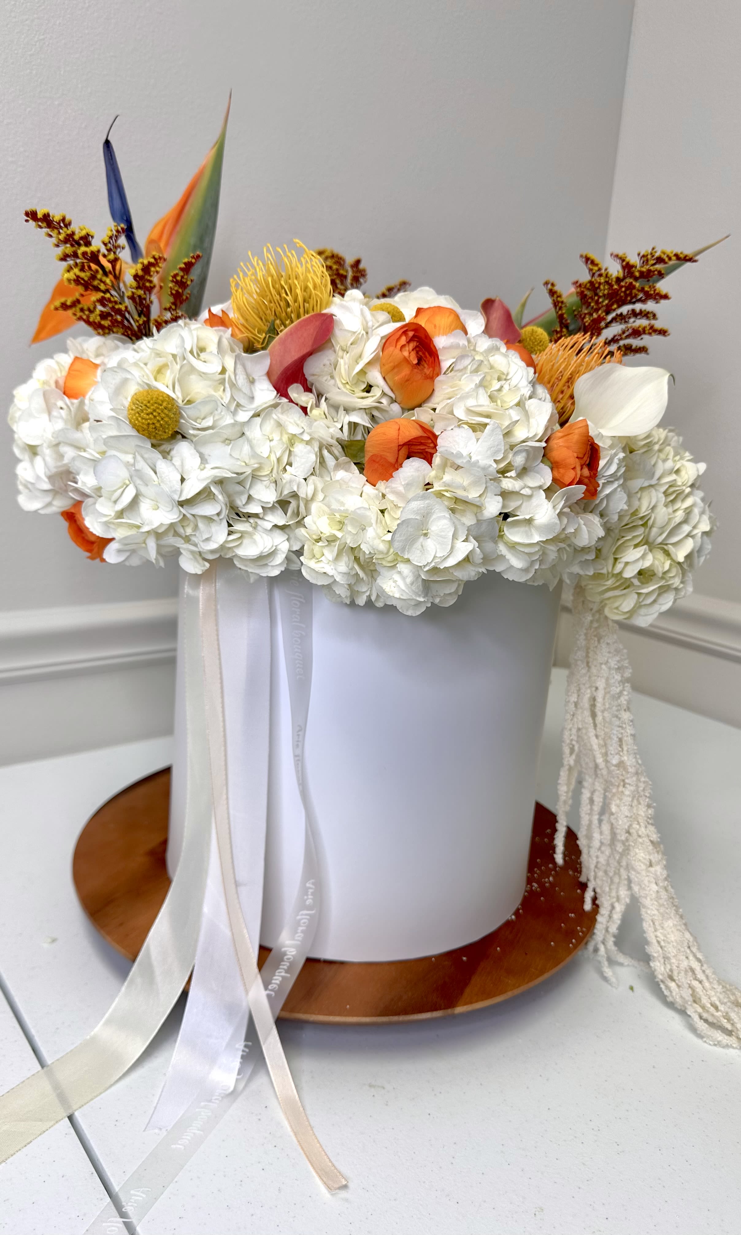 White floral arrangement with orange accents in a round white box