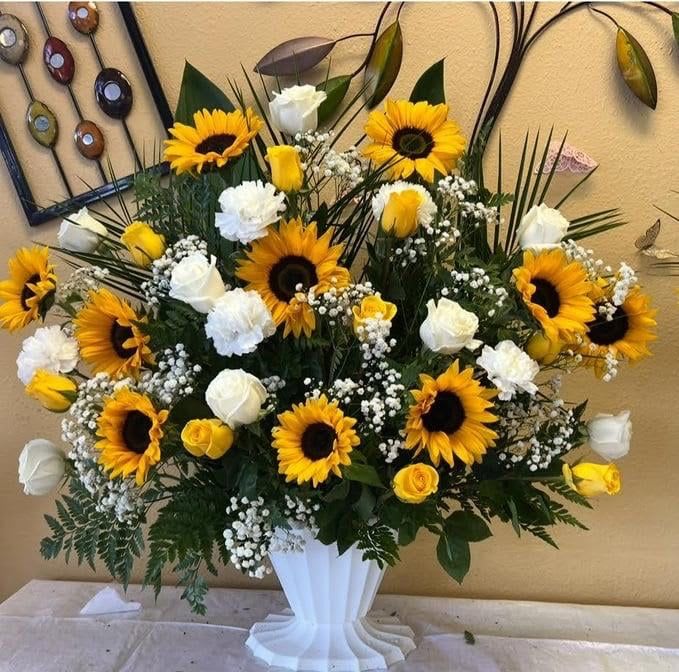 Large sunflower and white rose arrangement in a white pedestal vase