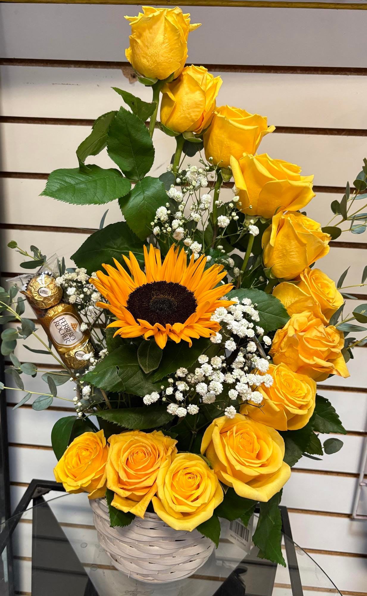 Yellow roses and a sunflower in a white basket with chocolates