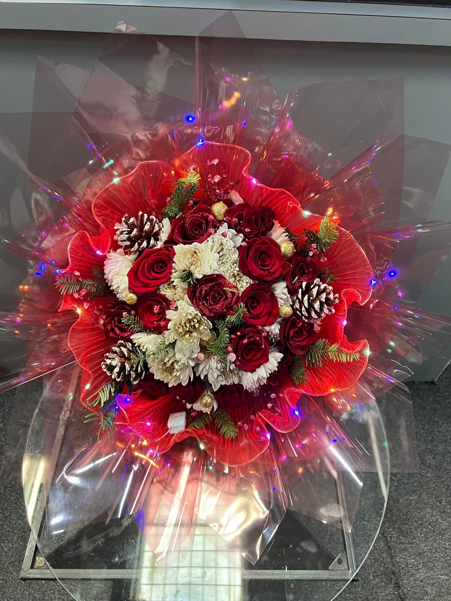Red and white rose bouquet with pinecones and lights in clear wrap