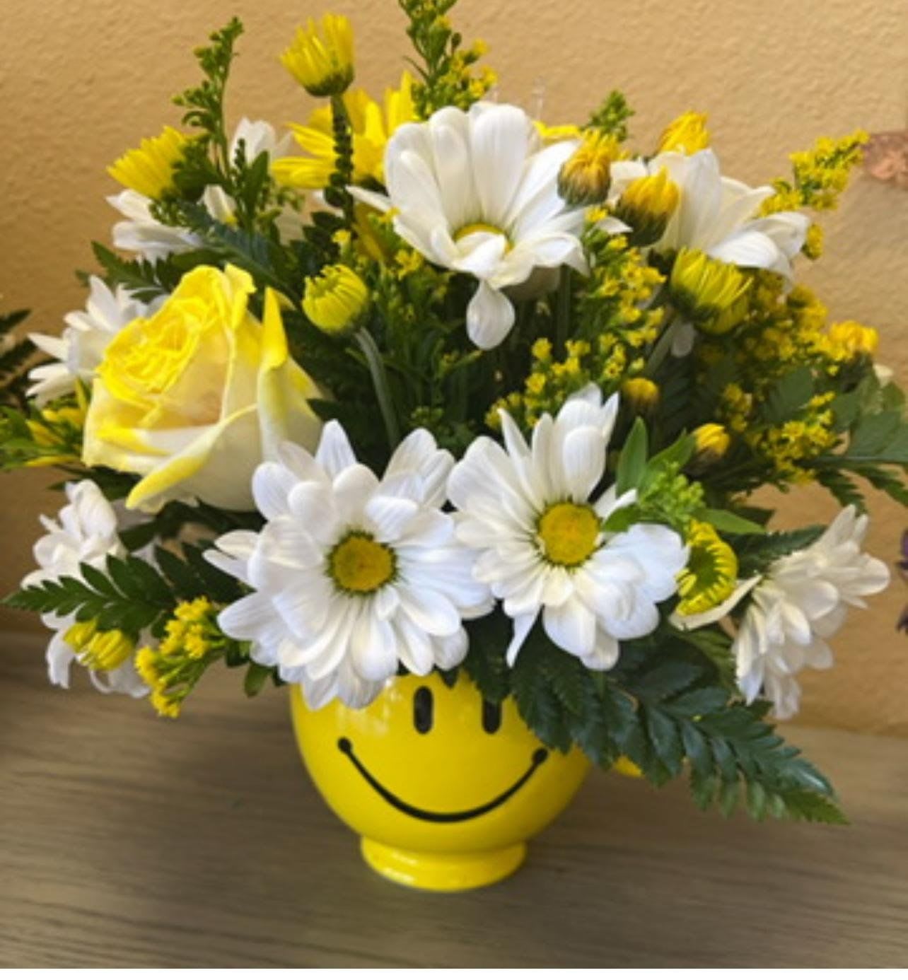 Yellow and white daisy bouquet in a smiley-face vase