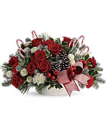 Red roses and white flowers in a low holiday centerpiece with candy canes and pinecones