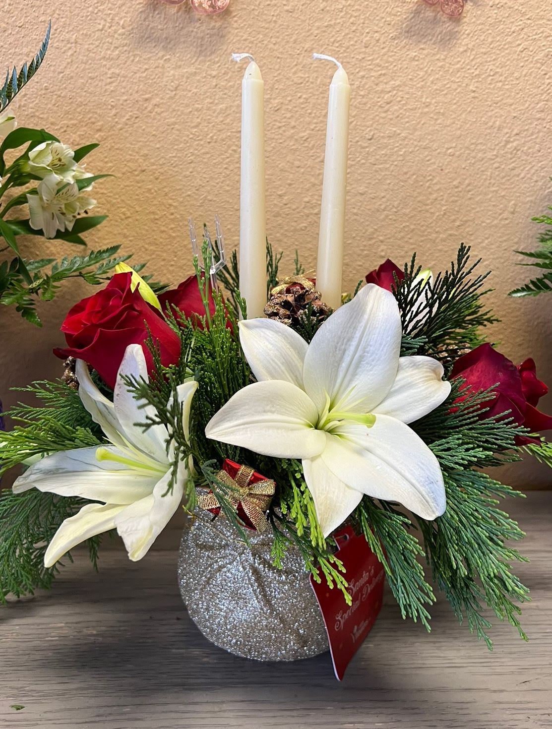 Holiday floral centerpiece with white lilies, red roses, and two taper candles