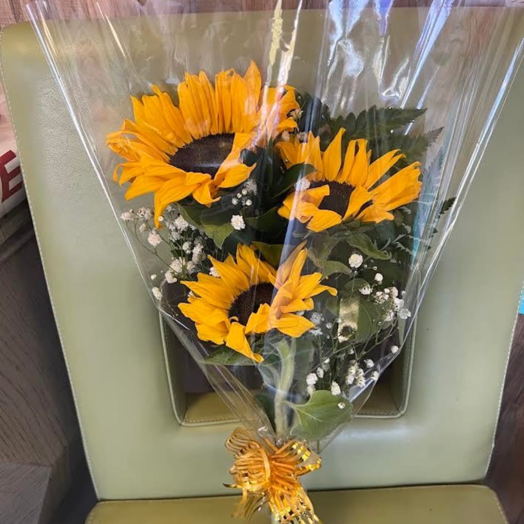 Bouquet of sunflowers wrapped in clear plastic with a gold ribbon