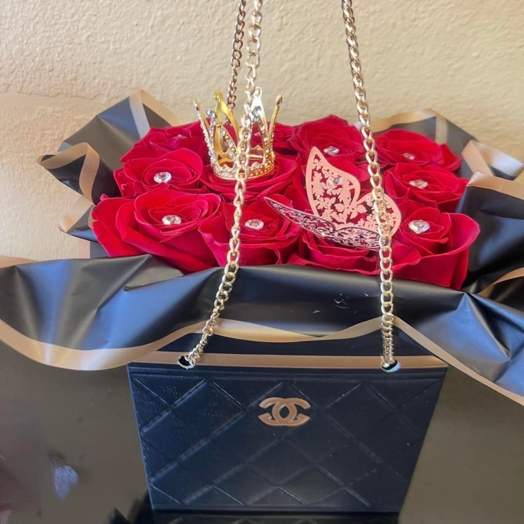 Red roses in a black gift box with gold chain handles and a crown topper
