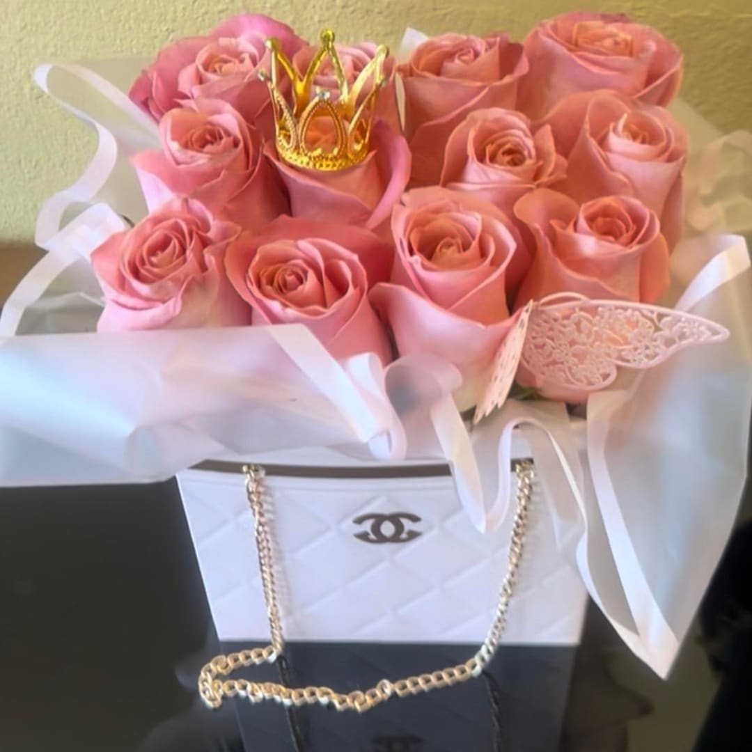 Pink roses arranged in a white gift bag with a small gold crown
