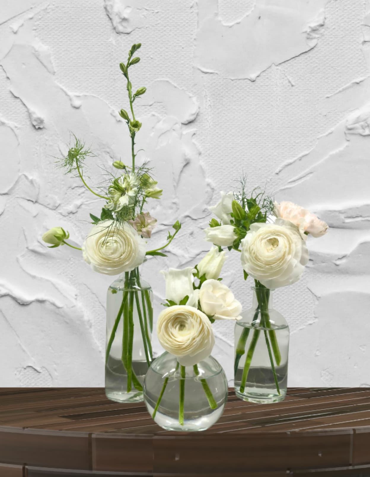 The Weekly Trio - "Hand-crafted by accredited Master Florist Tricia Won (AIFD, EMC, IMF) using premium seasonal market blooms. No two arrangements are identical."  The Weekly Trio: Ever-Changing, Always Elegant.  Elevate your floral standards with our signature Weekly Trio. We’ve designed these for the person who loves the "fine jewelry" of the floral world—the rare, the ruffled, and the architectural.  What’s Inside: Every week features a brand-new color story and seasonal curation. Each individual vase contains three premium focal stems artfully paired with delicate greenery or unique accents, ensuring each vessel feels like a complete, miniature masterpiece.  From Coffee Tables to Celebrations: While designed to bring a touch of luxury to your everyday spaces, the sophisticated scale and premium stem count make this trio a favorite for weddings and events. Whether you are decorating your kitchen island or styling a wedding reception, these vases offer professional-level floral design in a flexible, modular format.