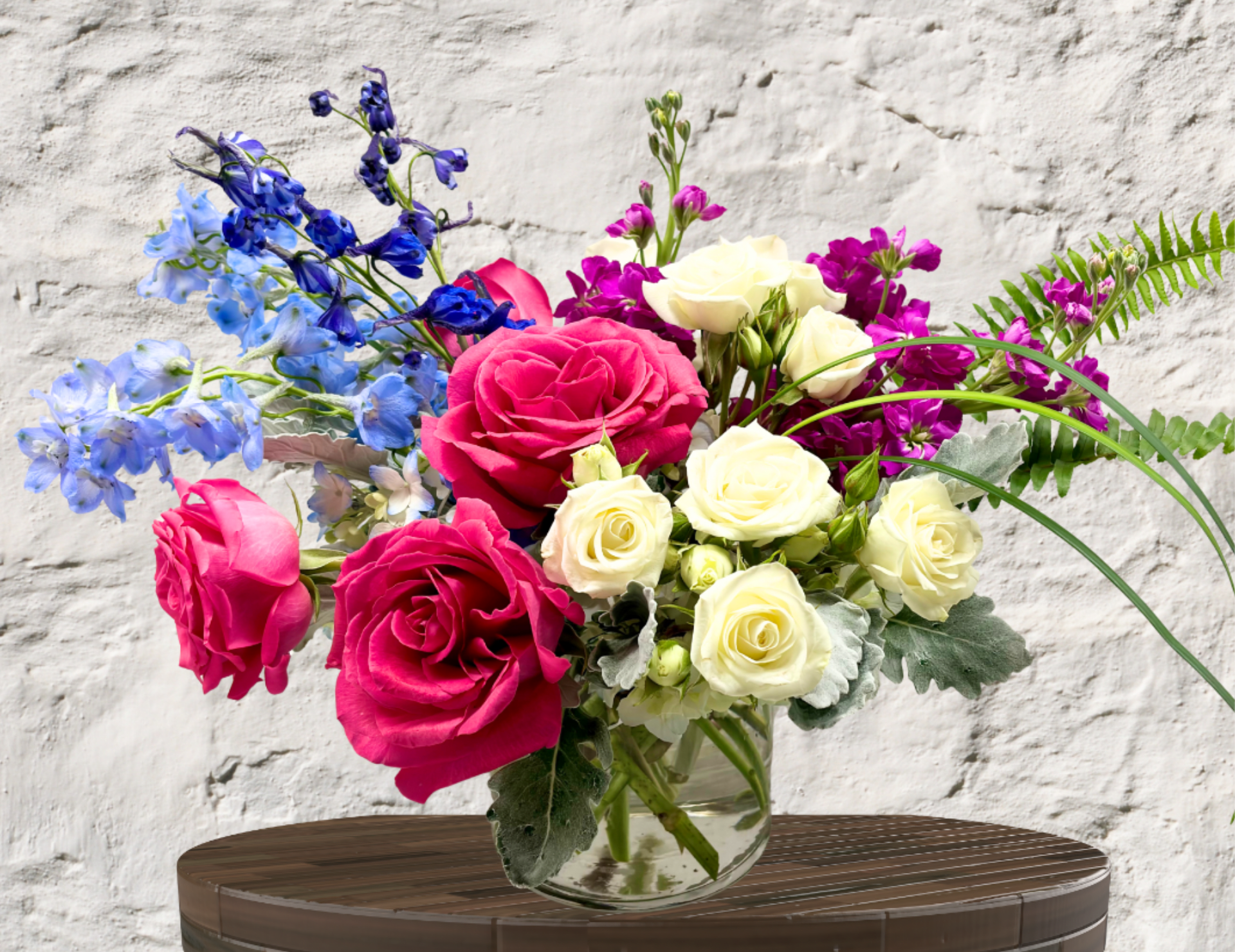 Boho Bliss - "Hand-crafted by accredited Master Florist Tricia Won (AIFD, EMC, IMF) using premium seasonal market blooms. No two arrangements are identical."  A Kaleidoscope of Coastal Romance  Break away from tradition with an arrangement that captures the wild, effortless beauty of a secret garden. Our Boho Bliss is a stunning multi-tonal masterpiece, perfect for someone who appreciates unique color palettes and rich textures.  Breathtaking Contrast: The rare combination of blue and hot pink creates a vibrant, eye-catching display.  Textural Variety: A mix of ruffled roses, spiky delphinium, and soft, velvety foliage provides a rich sensory experience.  Artisan Design: Hand-arranged in a low, clear glass vase, making it a perfect centerpiece that doesn't obstruct conversation.  It's a perfect gift for any occasion.      
