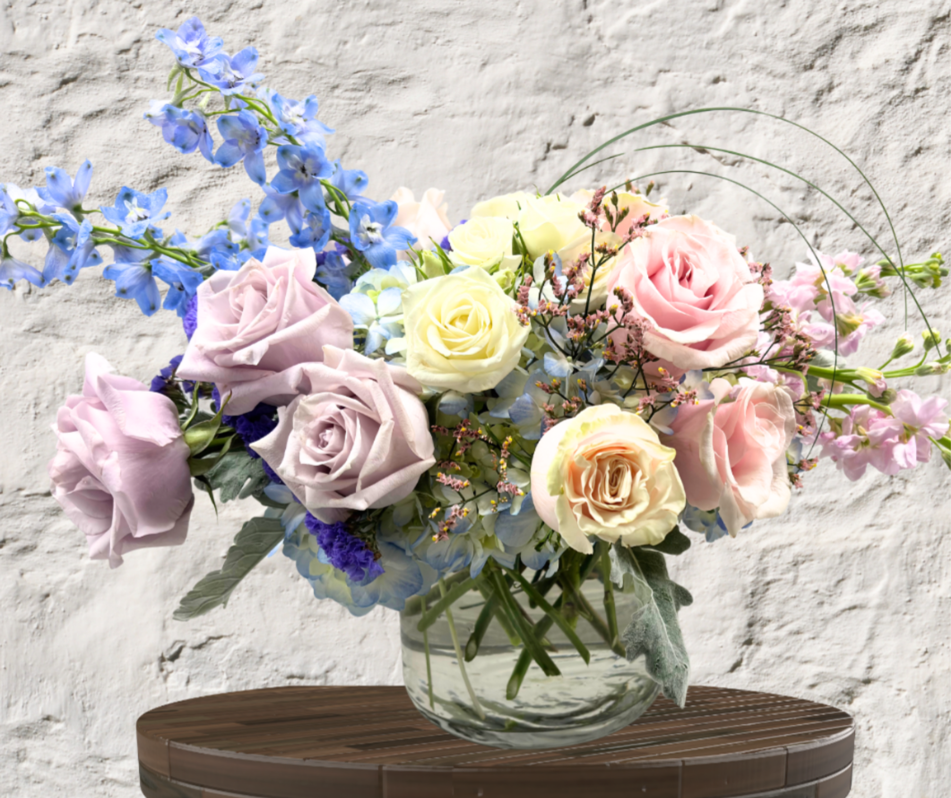 Pastel roses and blue flowers arranged in a clear glass vase