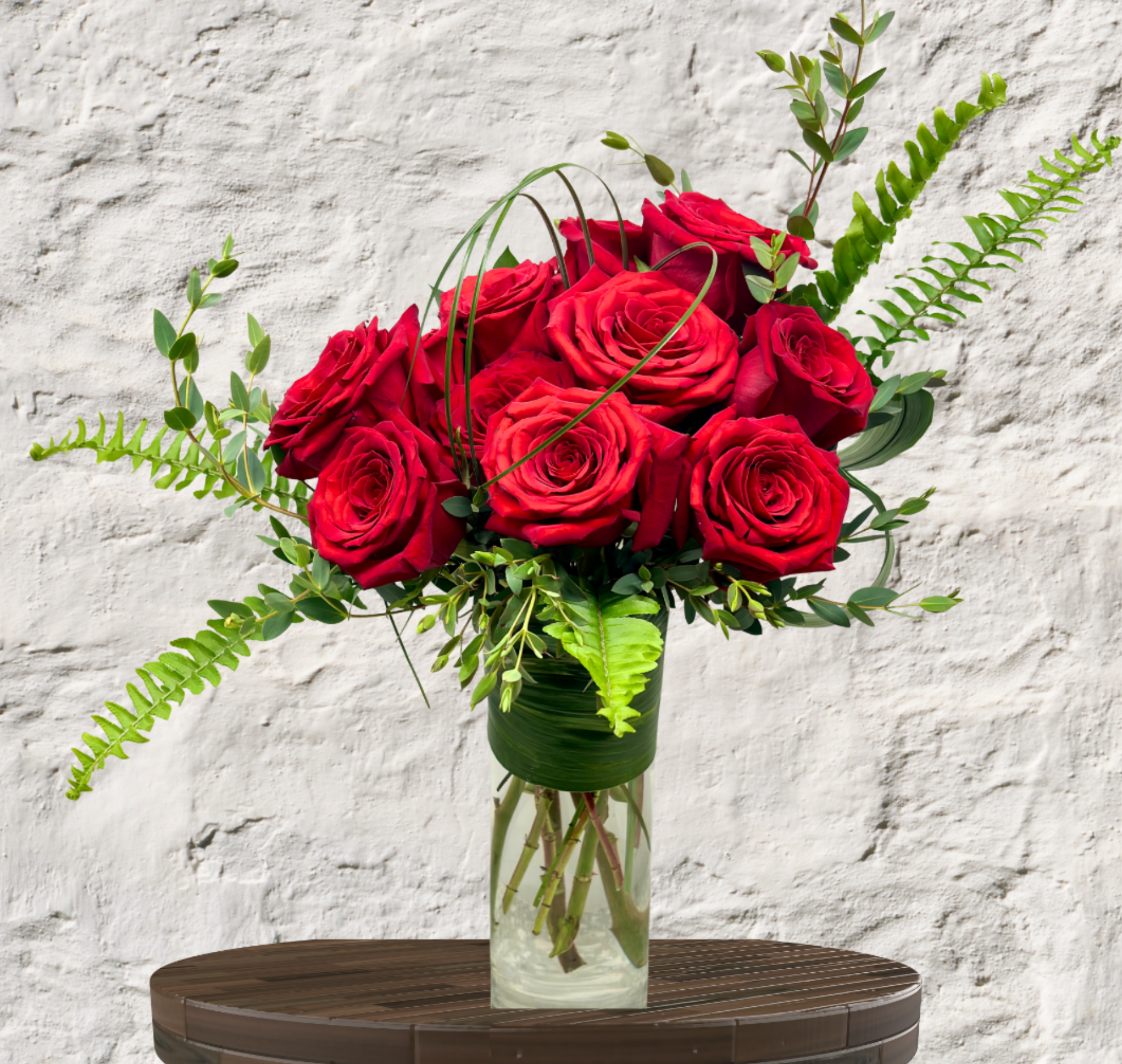 Red roses arranged in a clear glass vase with fern accents