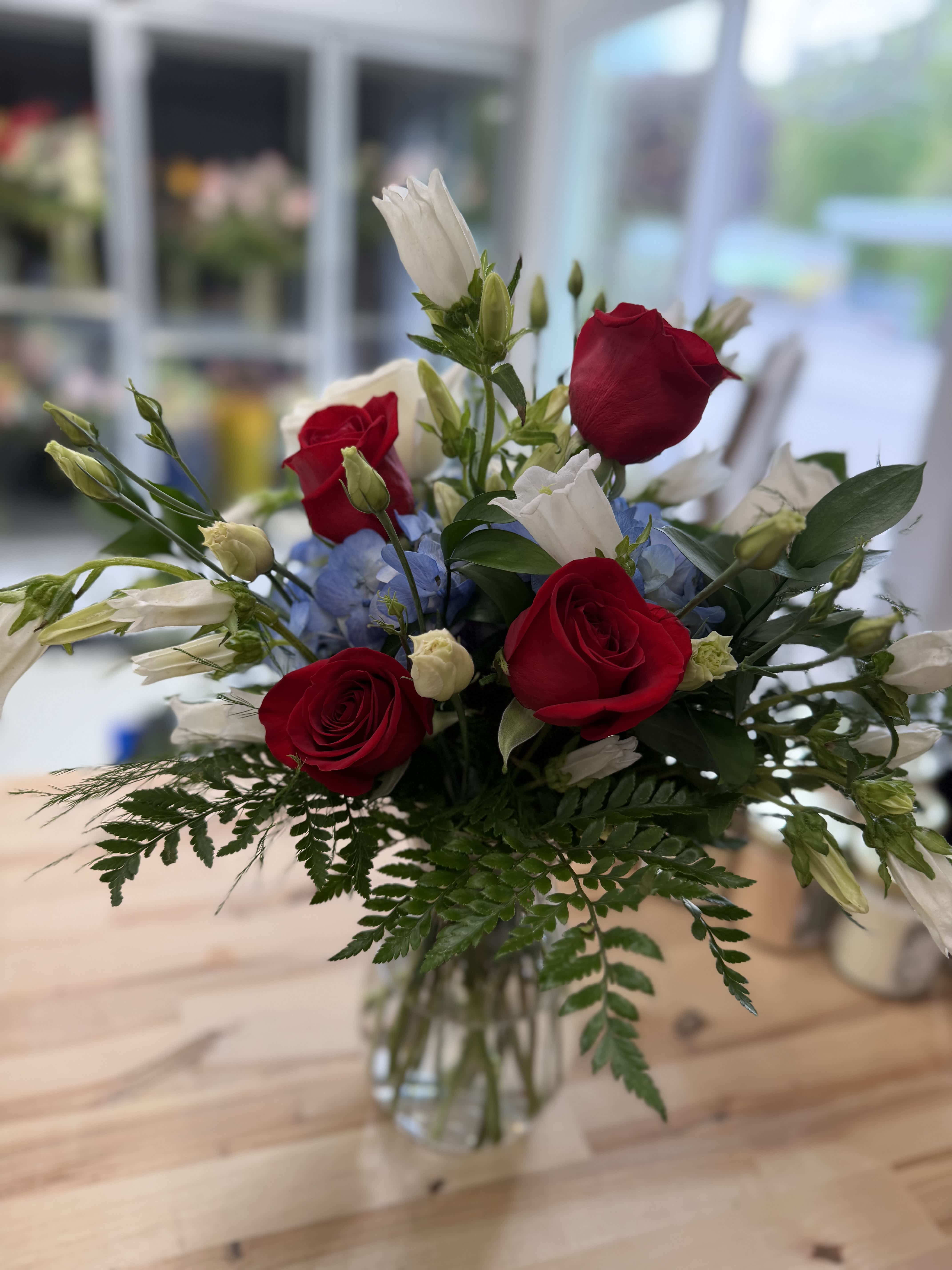 Bouquet of red roses, white bellflowers, and blue hydrangeas in a glass vase