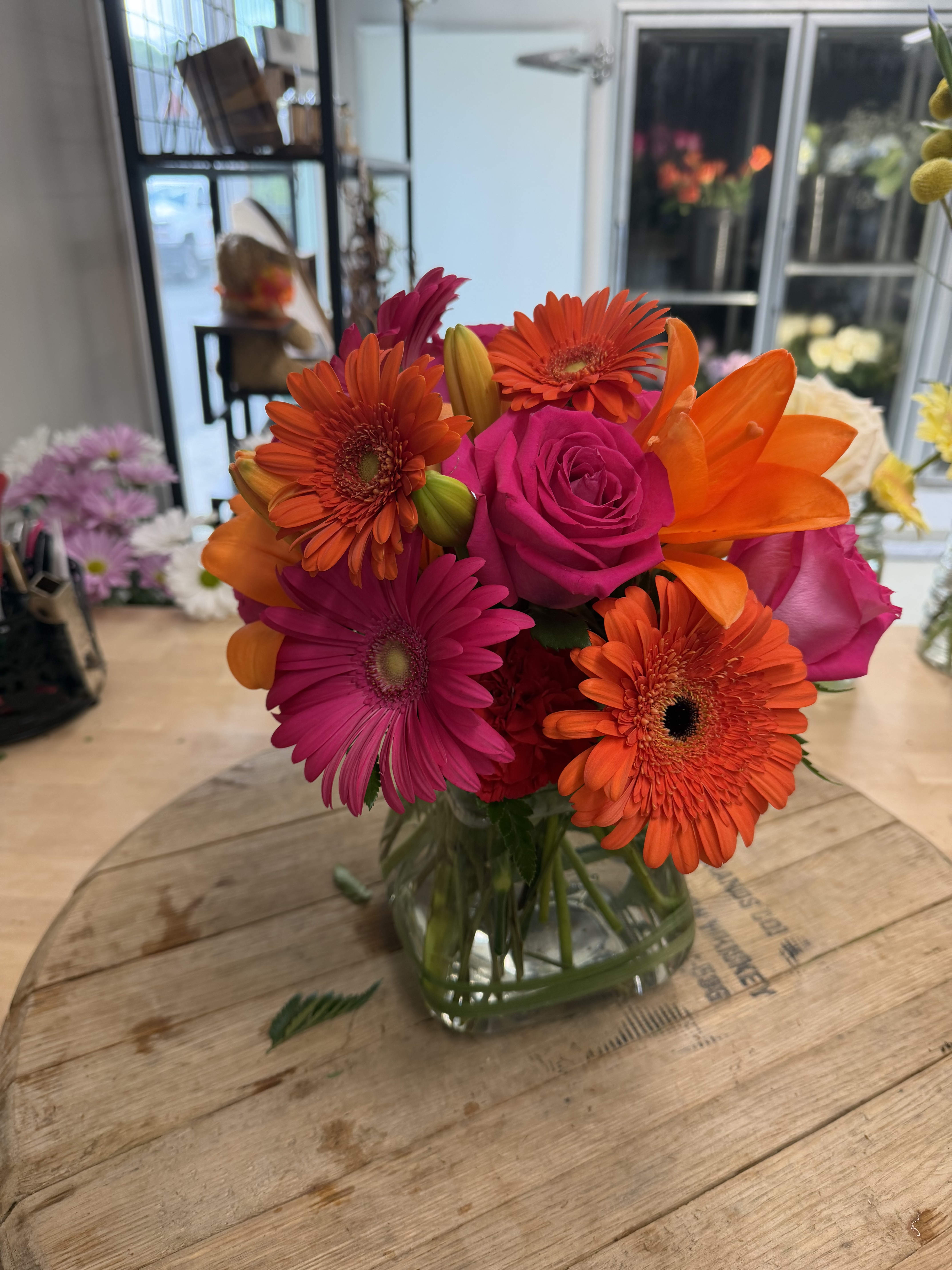 Bright mixed bouquet of pink roses, orange gerberas, and lilies in a glass vase