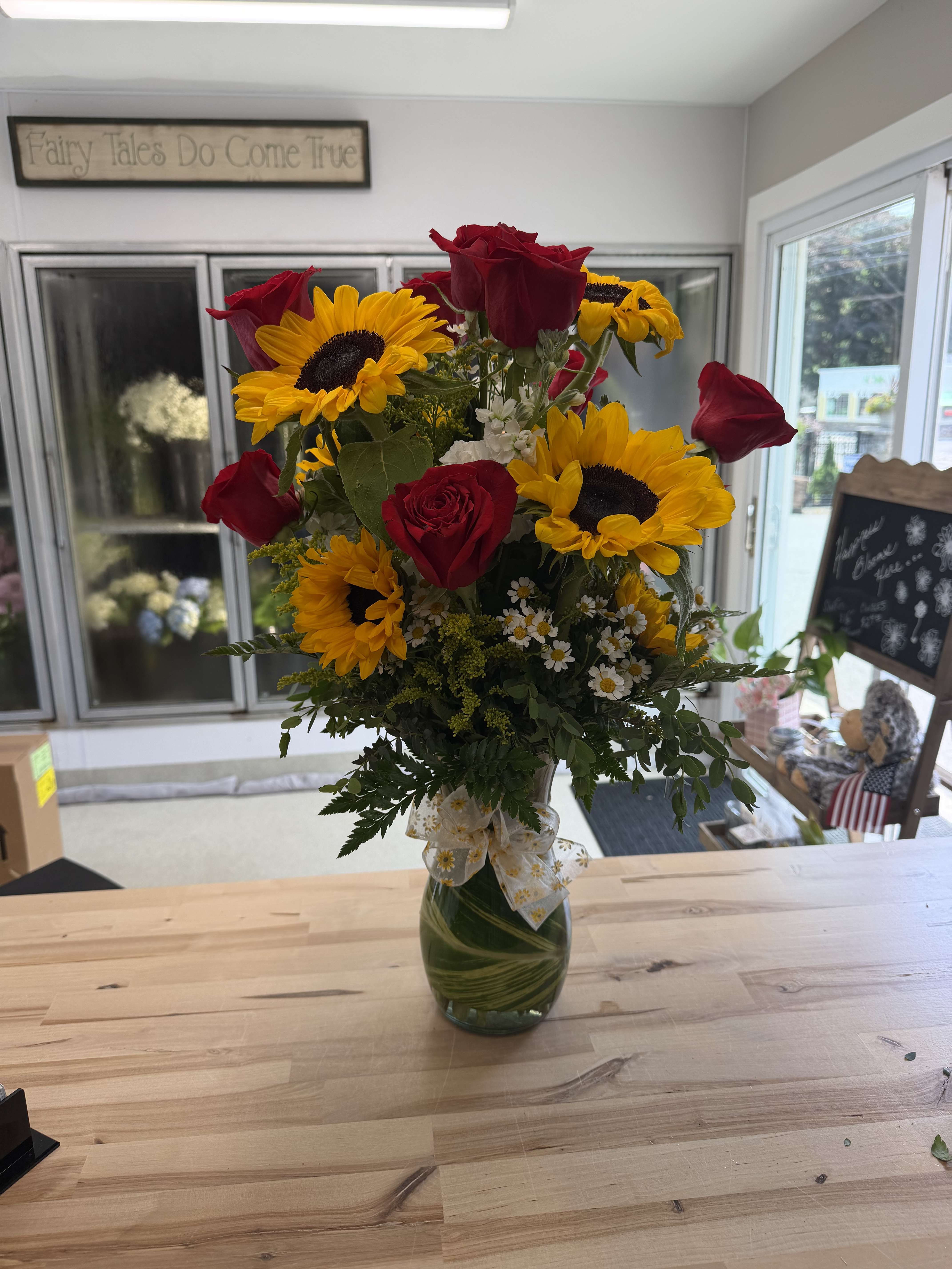 Red roses and yellow sunflowers in a glass vase with a ribbon