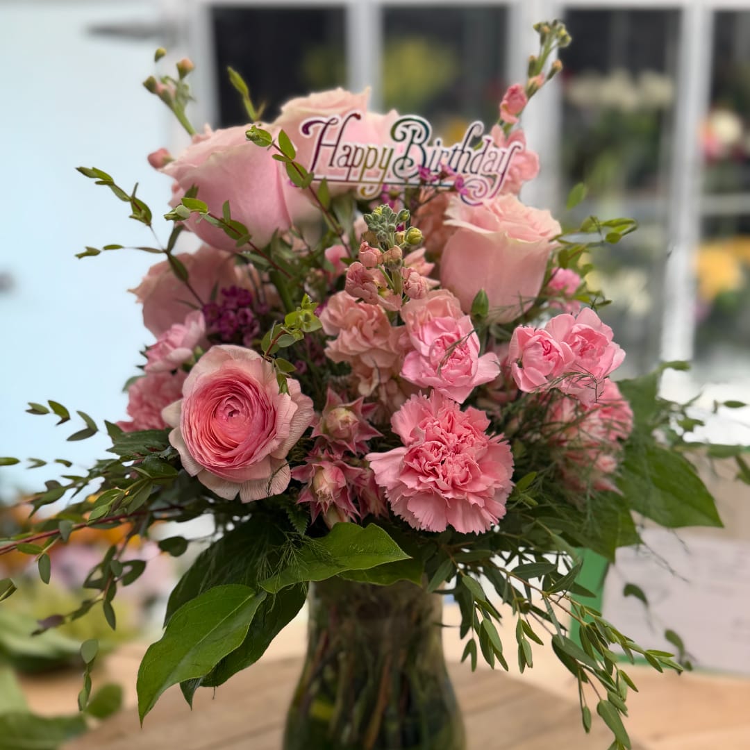Pink floral bouquet in a glass vase with a Happy Birthday sign