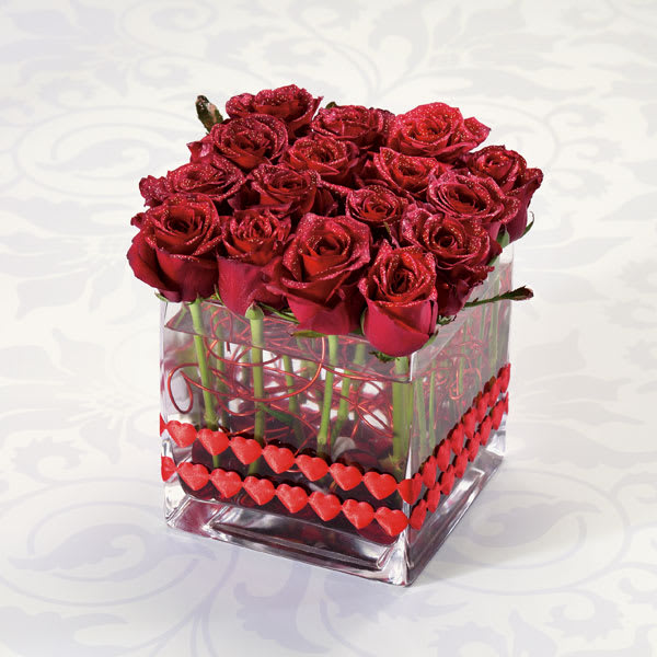 Square glass vase filled with glittered red roses and red heart accents.