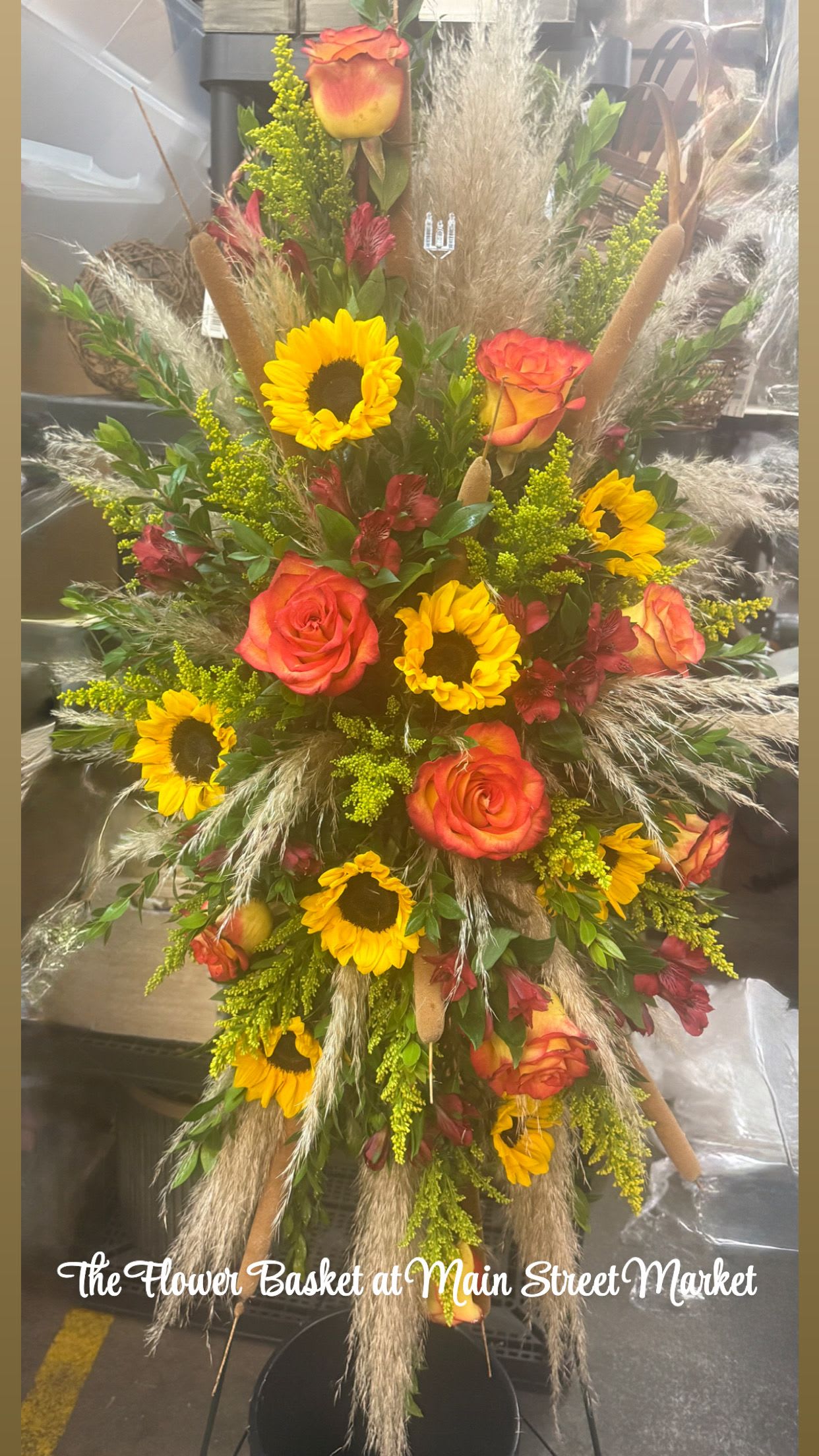 Tall arrangement of orange roses and sunflowers with dried grasses