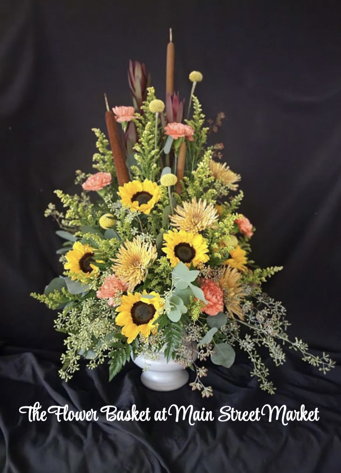 Tall floral arrangement with sunflowers, carnations, and a white vase