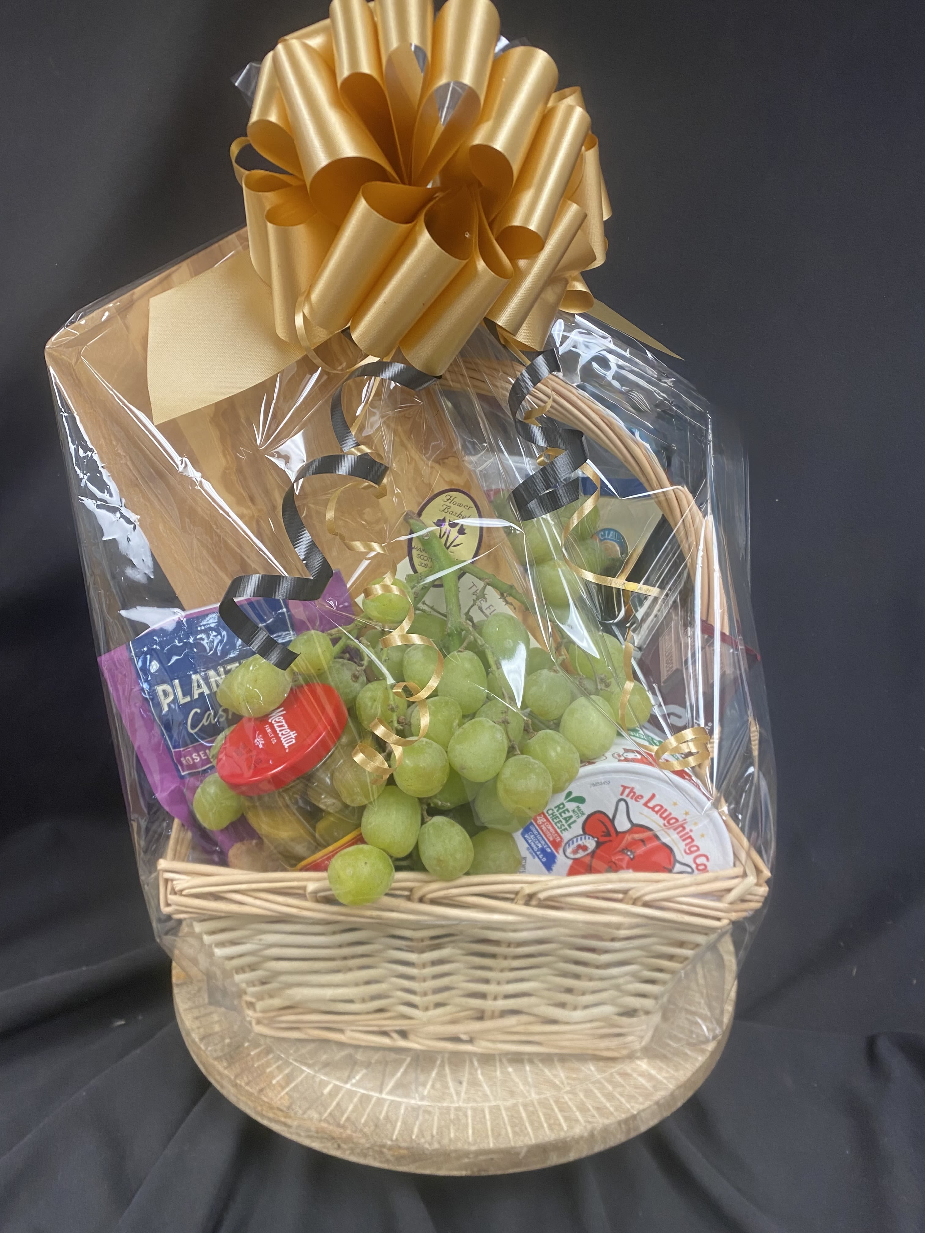 Gift basket with grapes, cheese, and crackers wrapped in cellophane with a gold bow