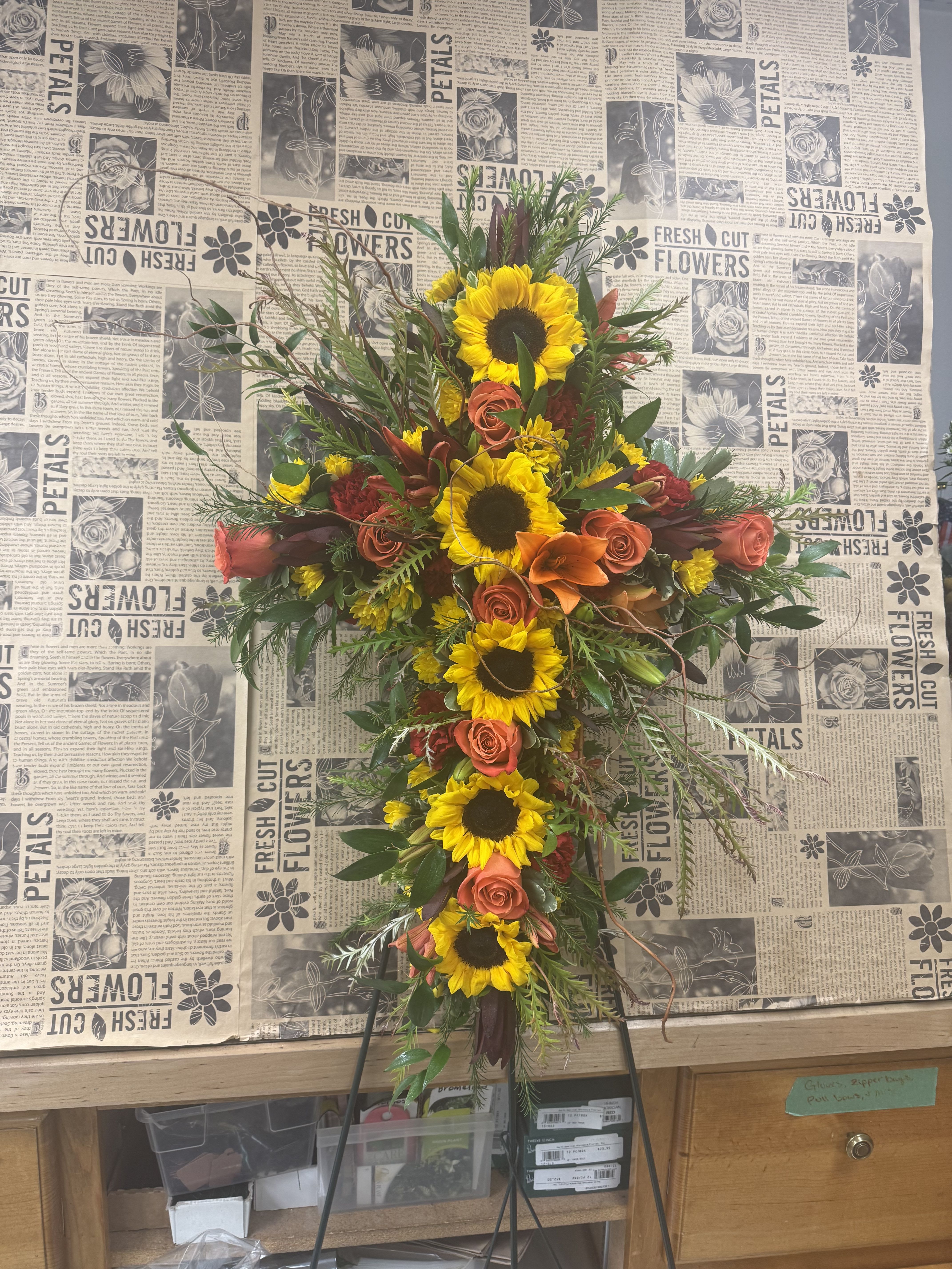 Cross-shaped floral spray with sunflowers, orange roses, and lilies