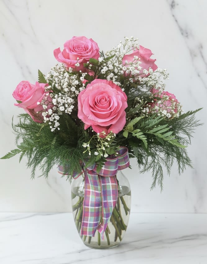 Pink roses in a glass vase with baby's breath and a plaid ribbon