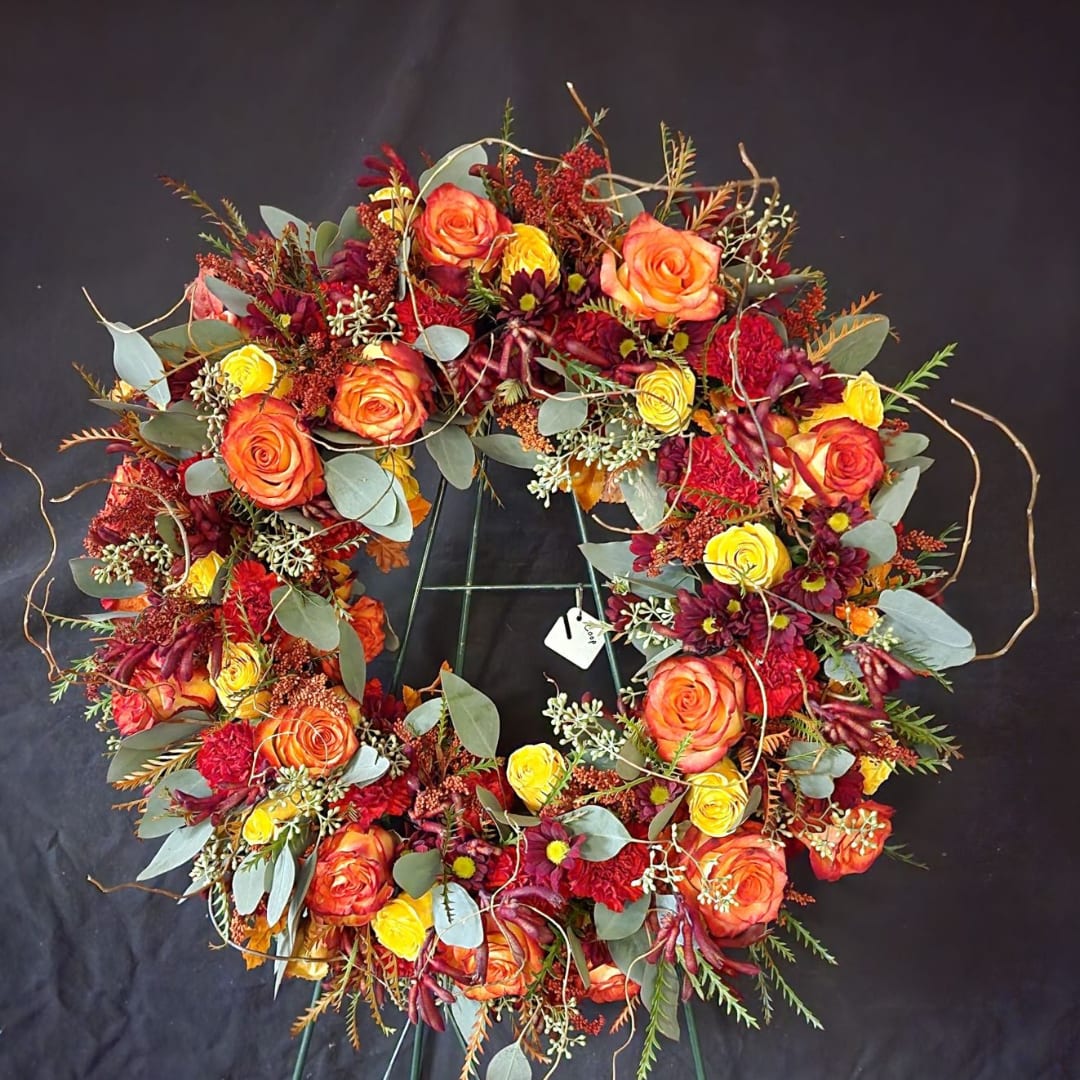 Circular floral wreath with orange and yellow roses on a black stand