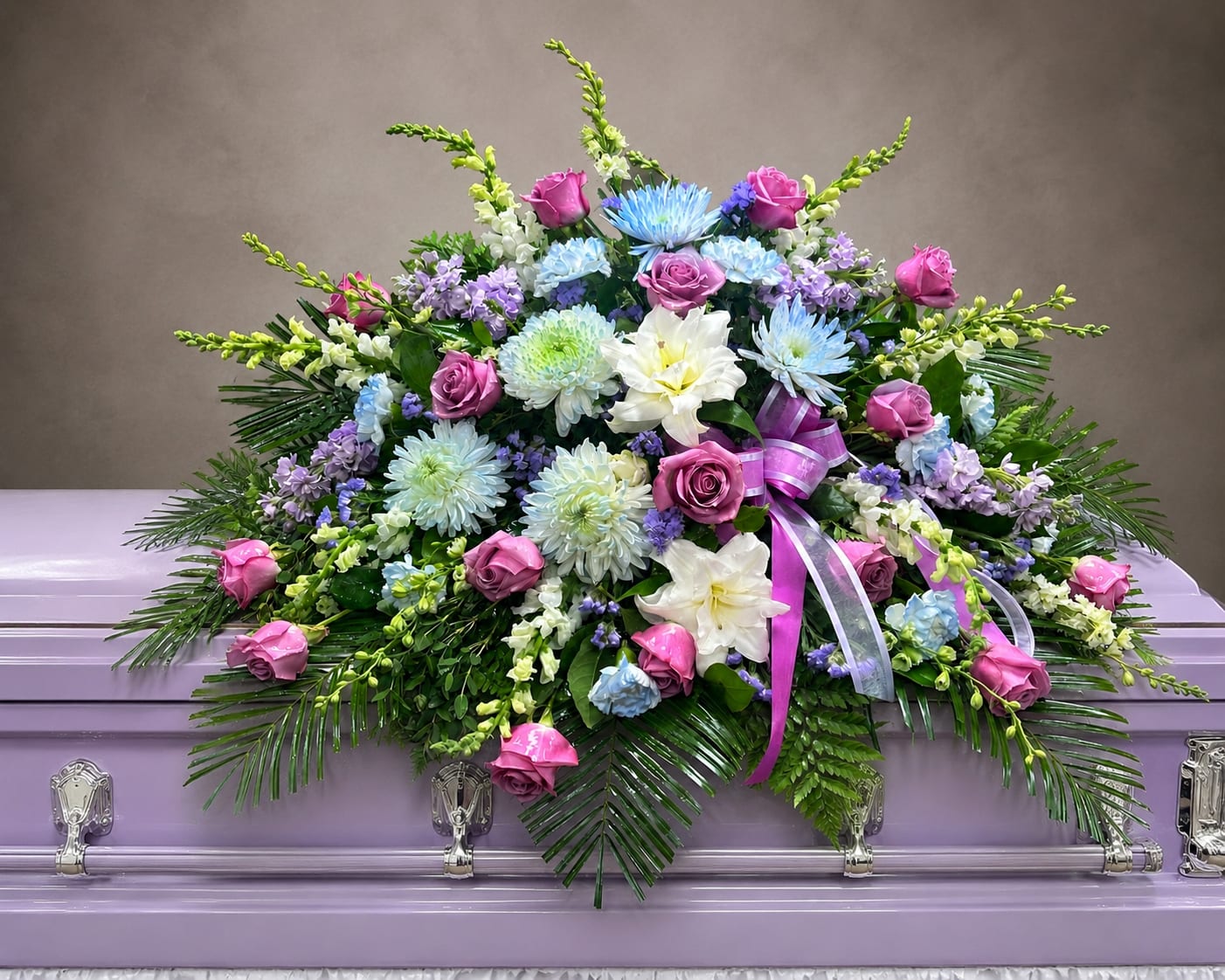 C25 Casket Spray - A mixture of white and lavender stock, lavender roses, white carnations tinted medium blue, whitesnap dragons, greens, and baby's breath, includes bow.  Banners are $15.00 + extra  Substitutions may apply, pending flower availability
