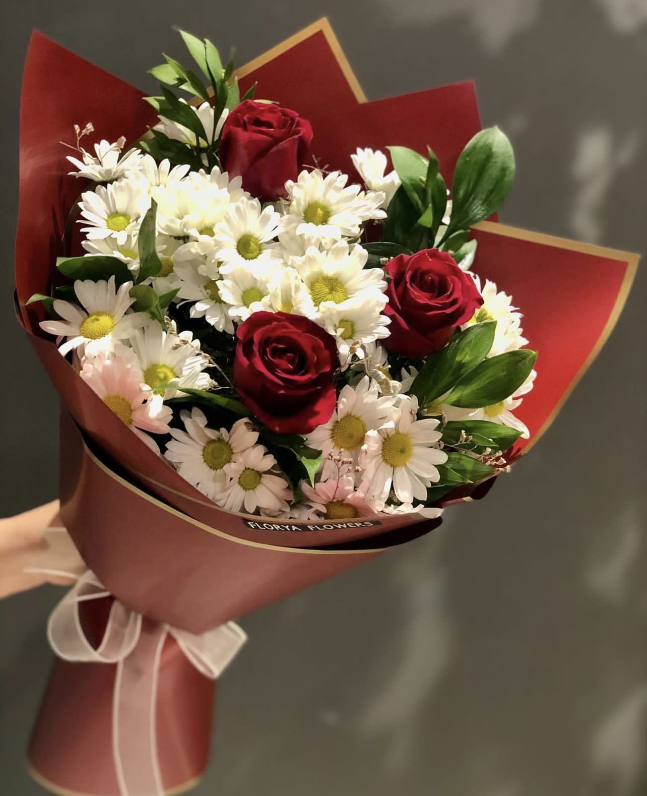Bouquet of red roses and white daisies wrapped in burgundy paper