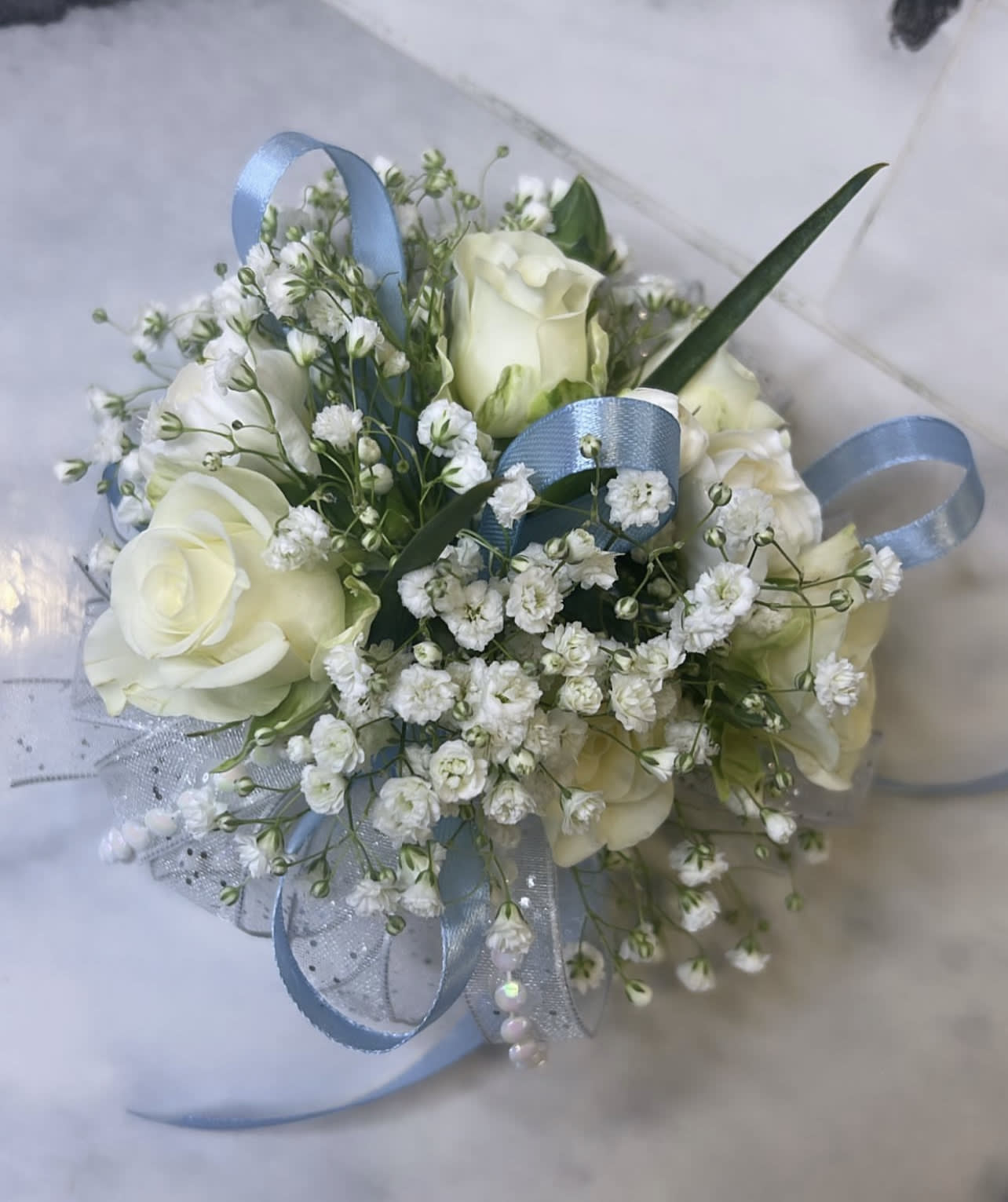 Small cluster of ivory roses and tiny white blooms with blue ribbon accents.