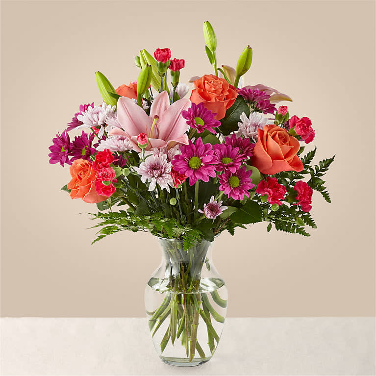 The Light of My Life Bouquet - LIGHT OF MY LIFE BOUQUET  The Light of My Life Bouquet blossoms with brilliant color and a sweet sophistication to create the perfect impression! Pink Lilies make the eyes dance across the unique design of this flower bouquet, surrounded by the blushing colors of orange roses, lavender cushion poms, hot pink carnations, and lush greens. Presented in a clear glass vase, this fresh flower arrangement has been created just for you to help you send your sweetest thank you, happy anniversary, or thinking of you wishes.  Please Note: The bouquet pictured reflects our original design for this product. While we always try to follow the color palette, we may replace stems to deliver the freshest bouquet possible, and we may sometimes need to use a different vase.  DETAILS  