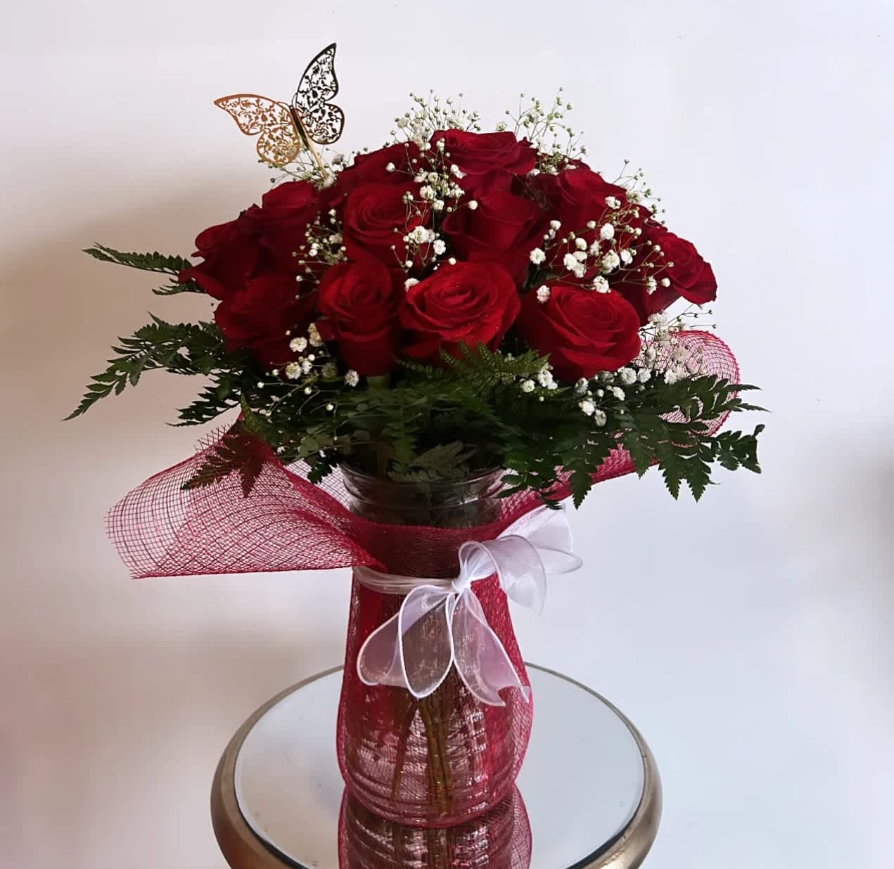 Red roses arranged in a clear vase with baby's breath and a white ribbon